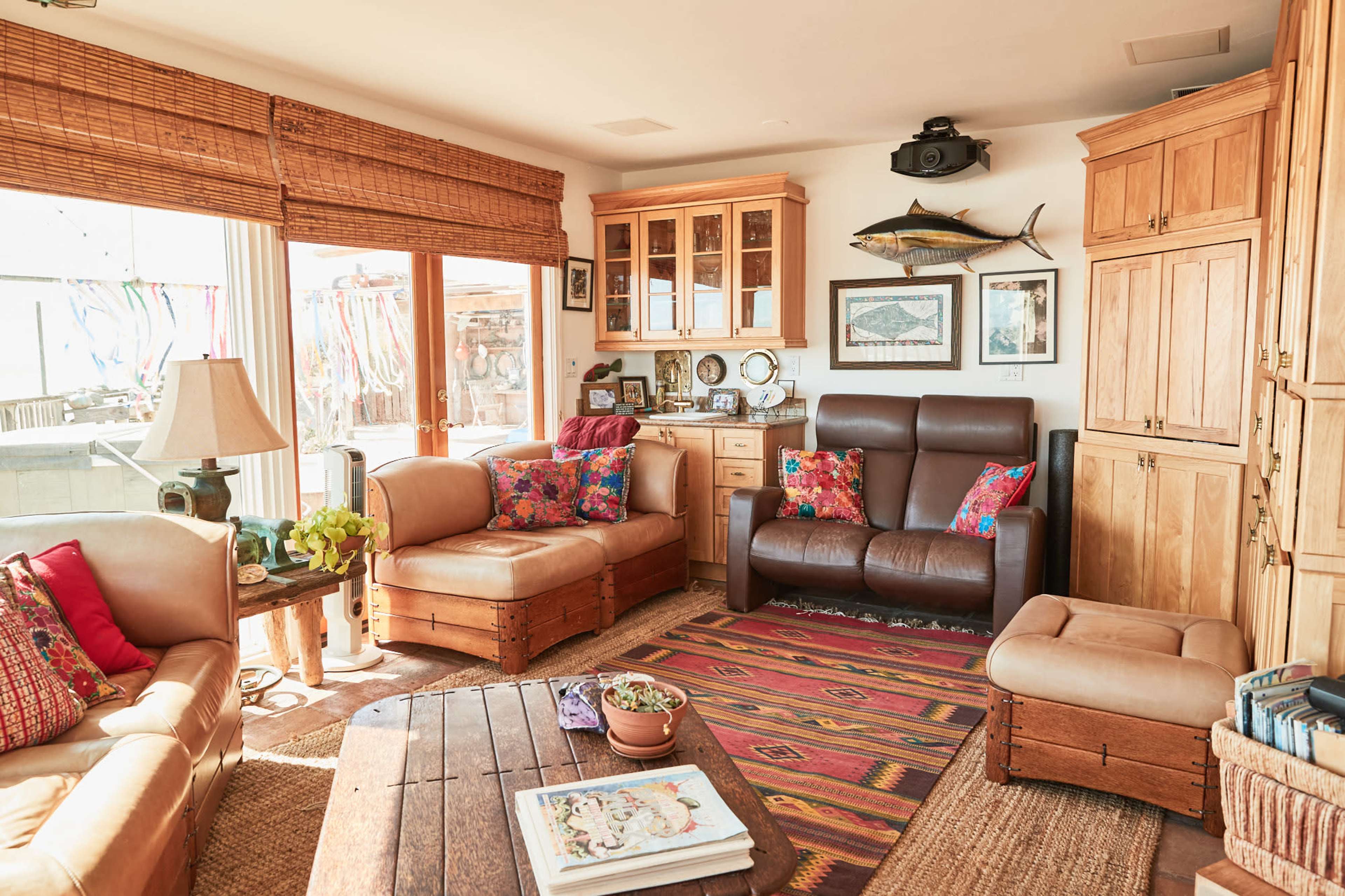 A cozy living room with wooden furniture, colorful cushions, and large windows allowing natural light.