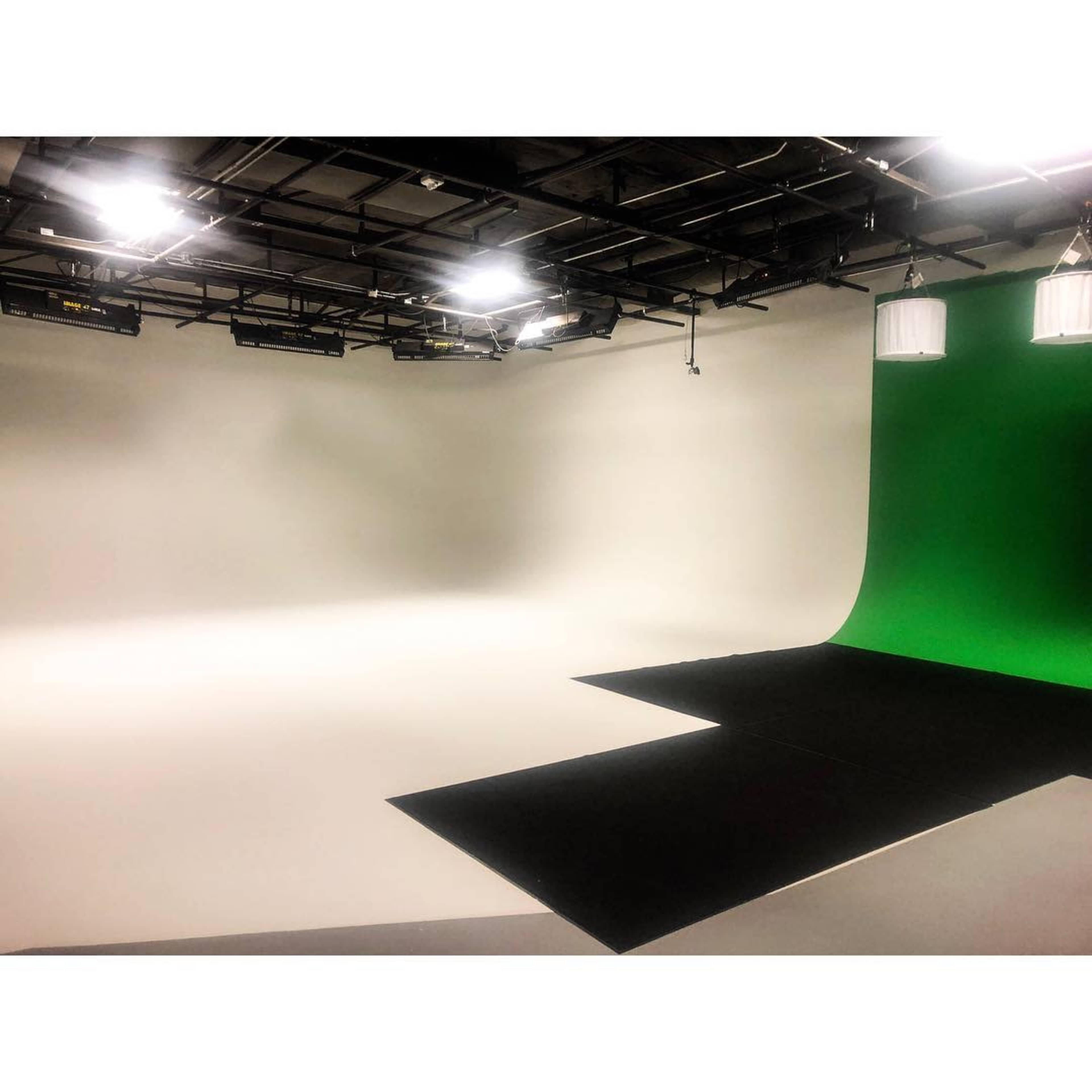 A photo studio featuring a green screen, black flooring, and a blank white backdrop.
