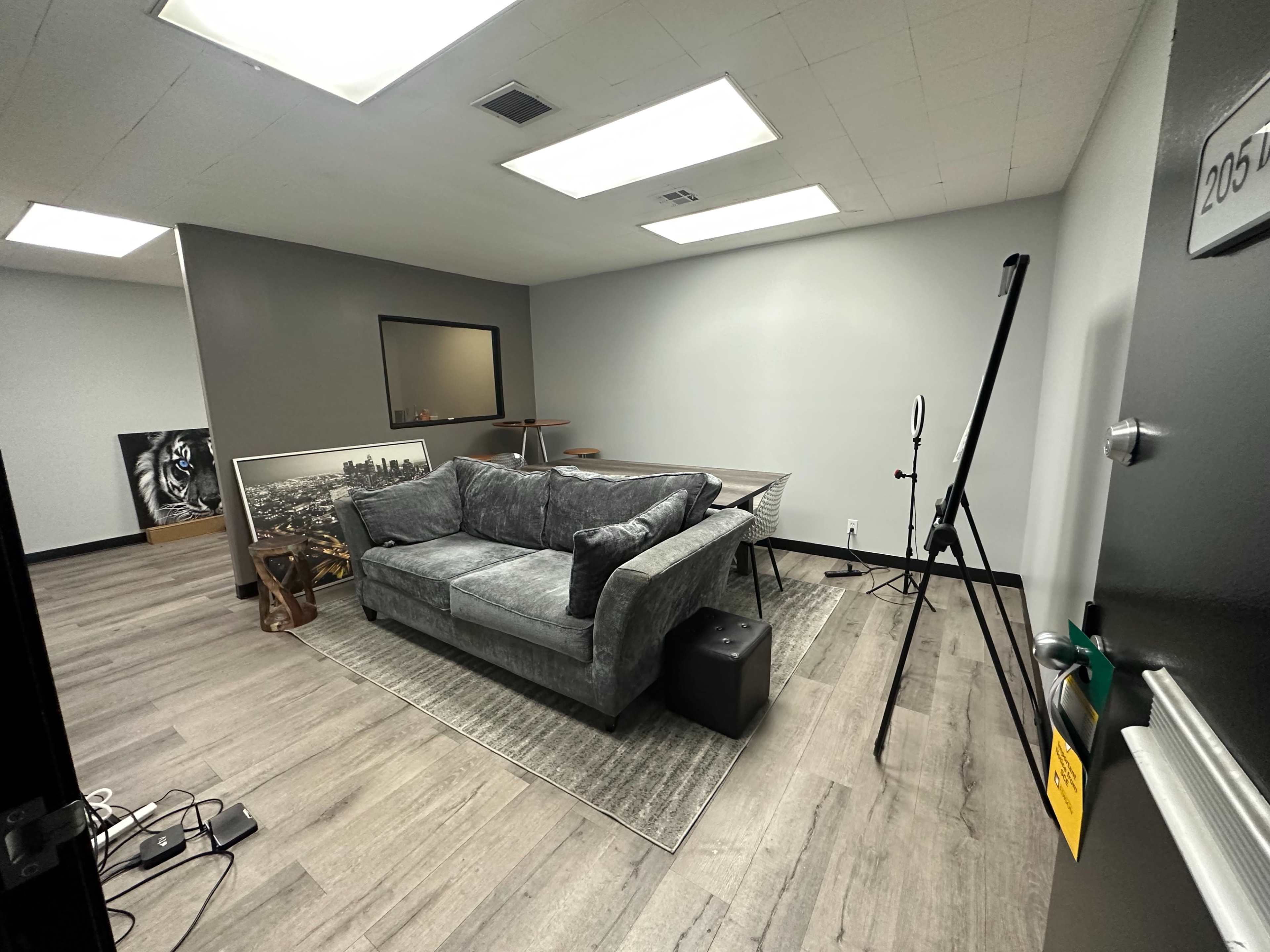 A gray sofa is placed in a sparsely decorated room with wooden floors, a table, and a mirror on the wall.