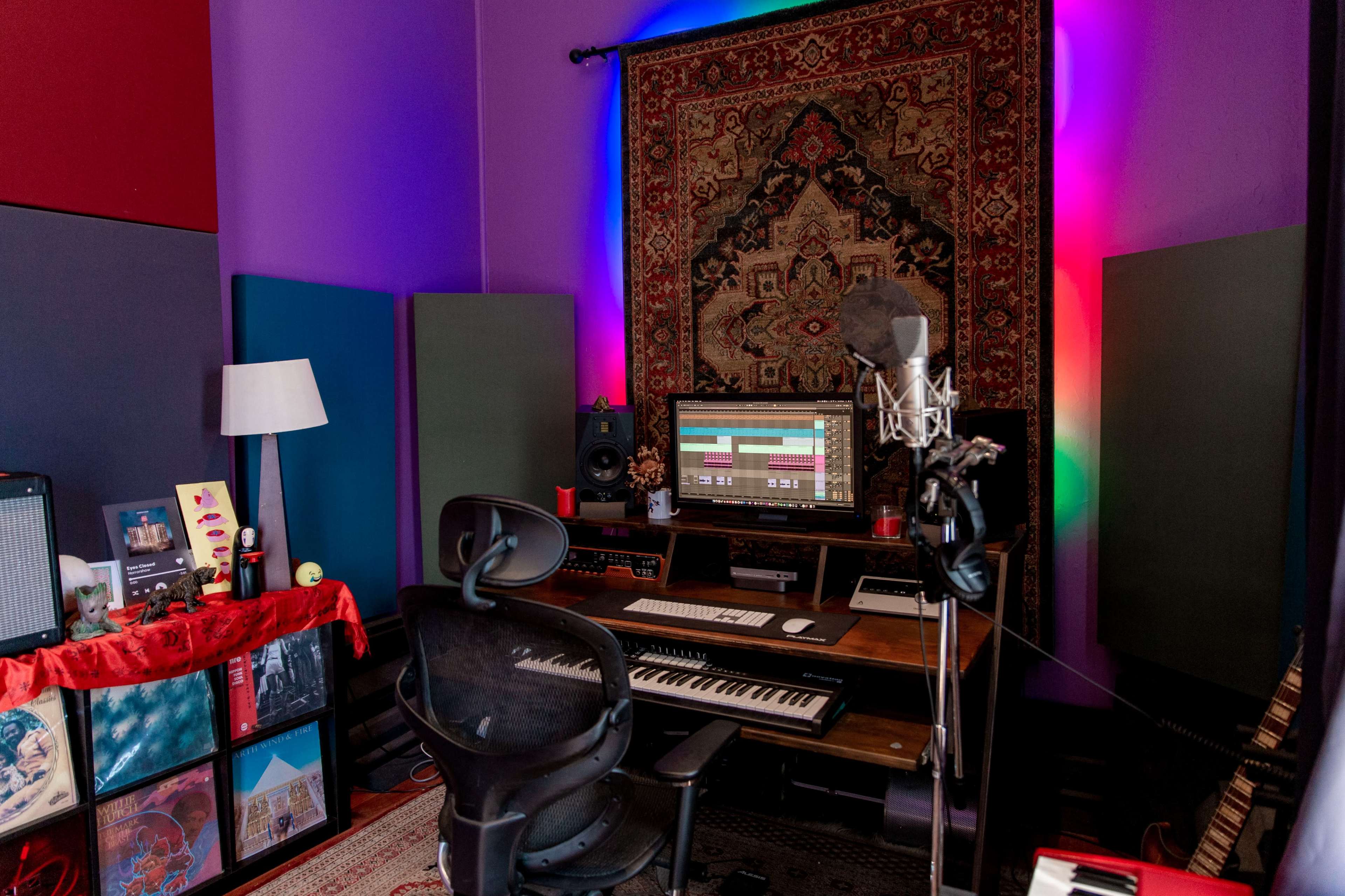 A music production studio features a microphone in front of a computer setup, surrounded by soundproofing panels and decorative lighting.