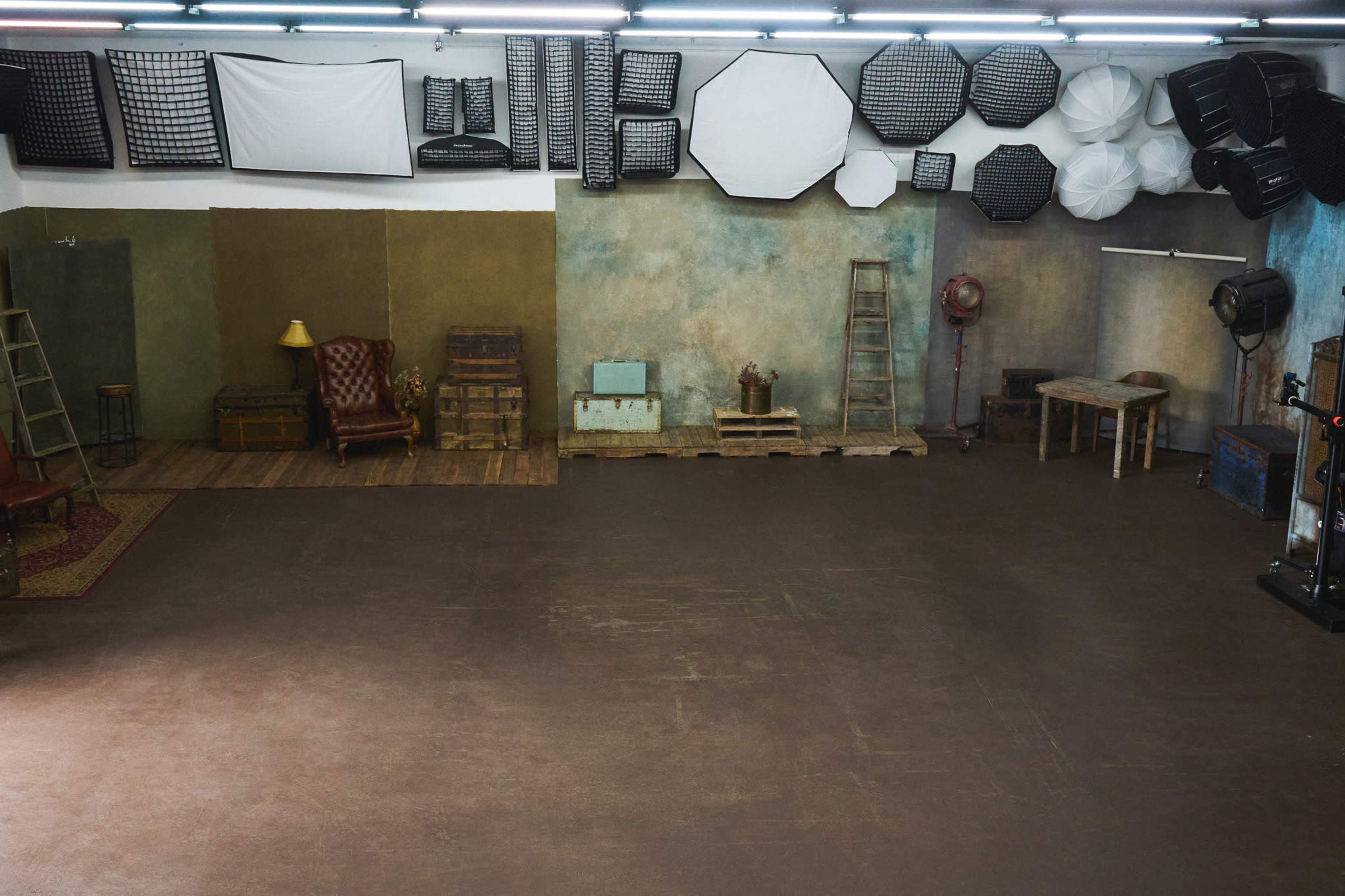 A spacious photography studio features various backdrops and lighting equipment, with furniture arranged in the corner.