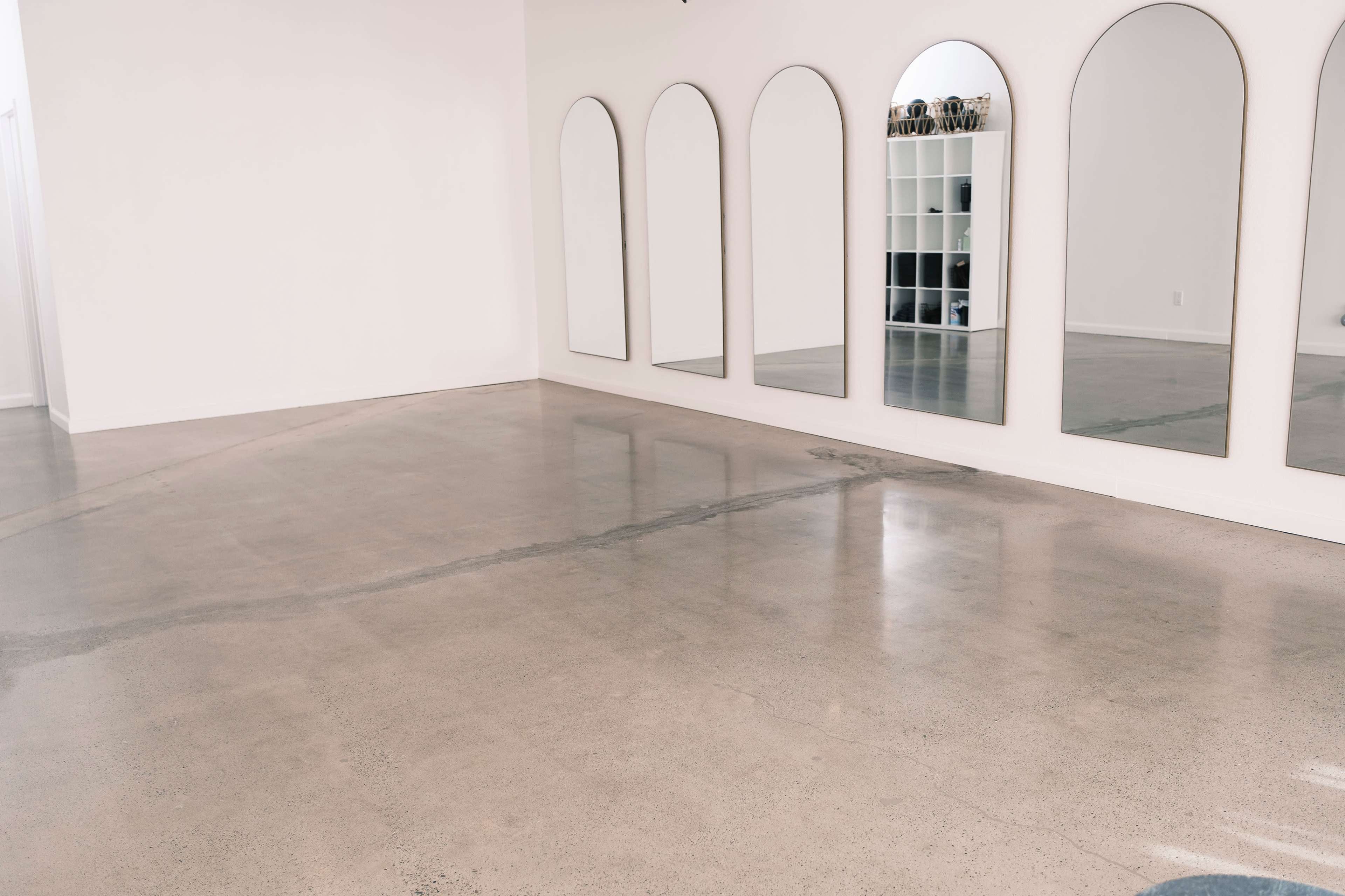 A spacious room with polished concrete flooring and several arched mirrors mounted on the wall.