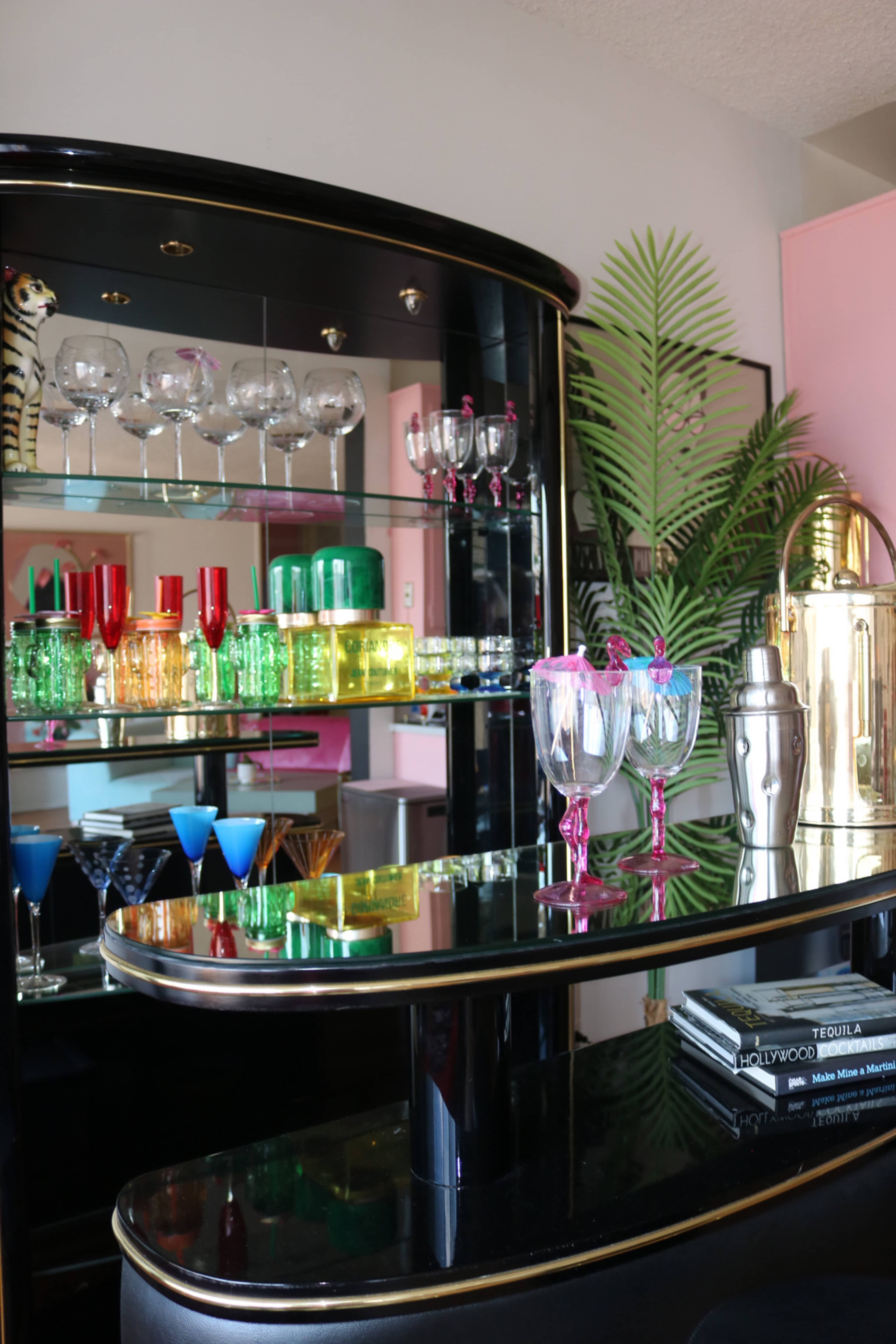 A modern bar cart displays an array of colorful glassware and cocktail accessories against a softly lit background.