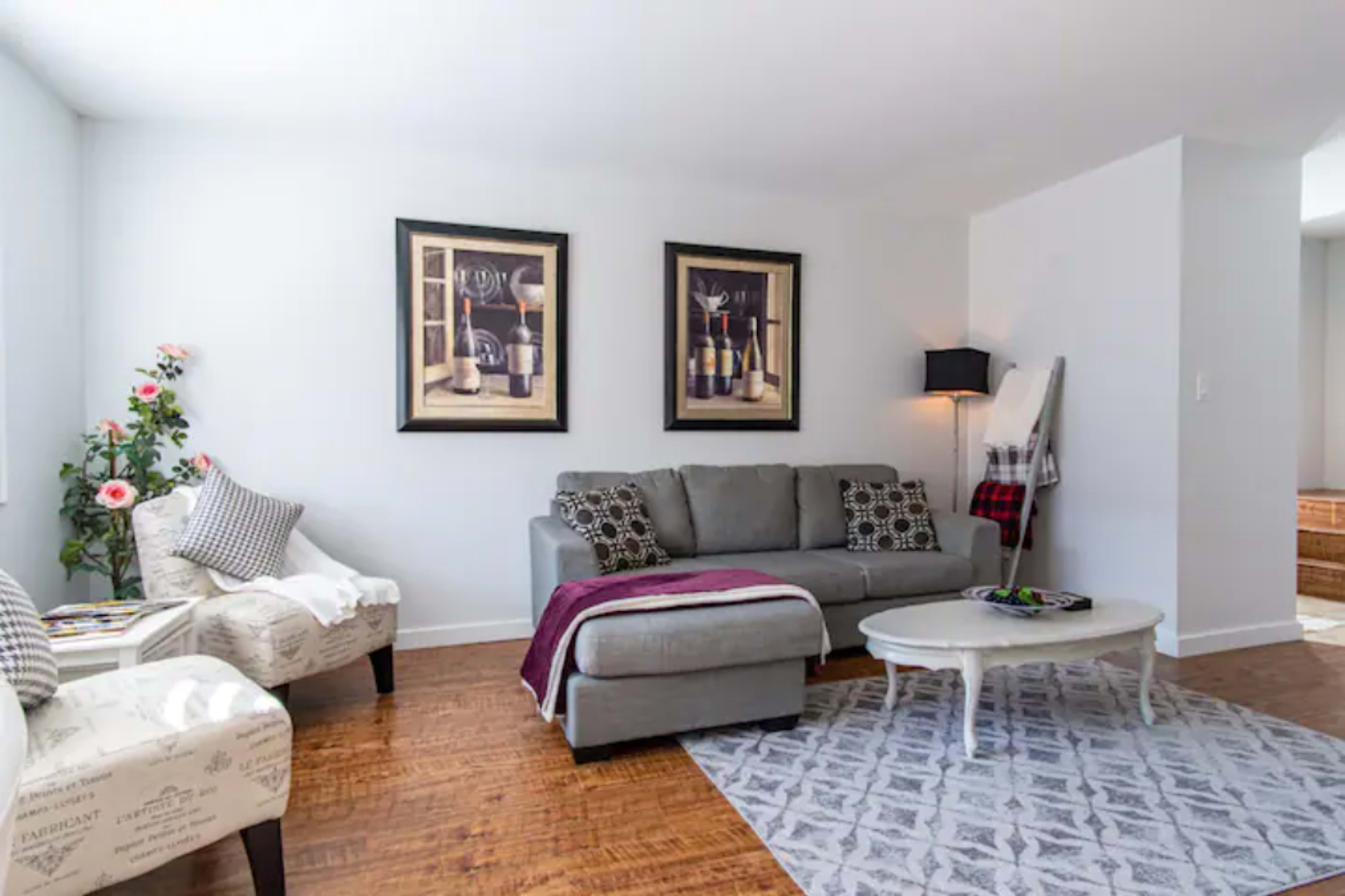 The living room features a gray sofa with a throw blanket, two patterned chairs, a round coffee table, and framed artwork on the walls.