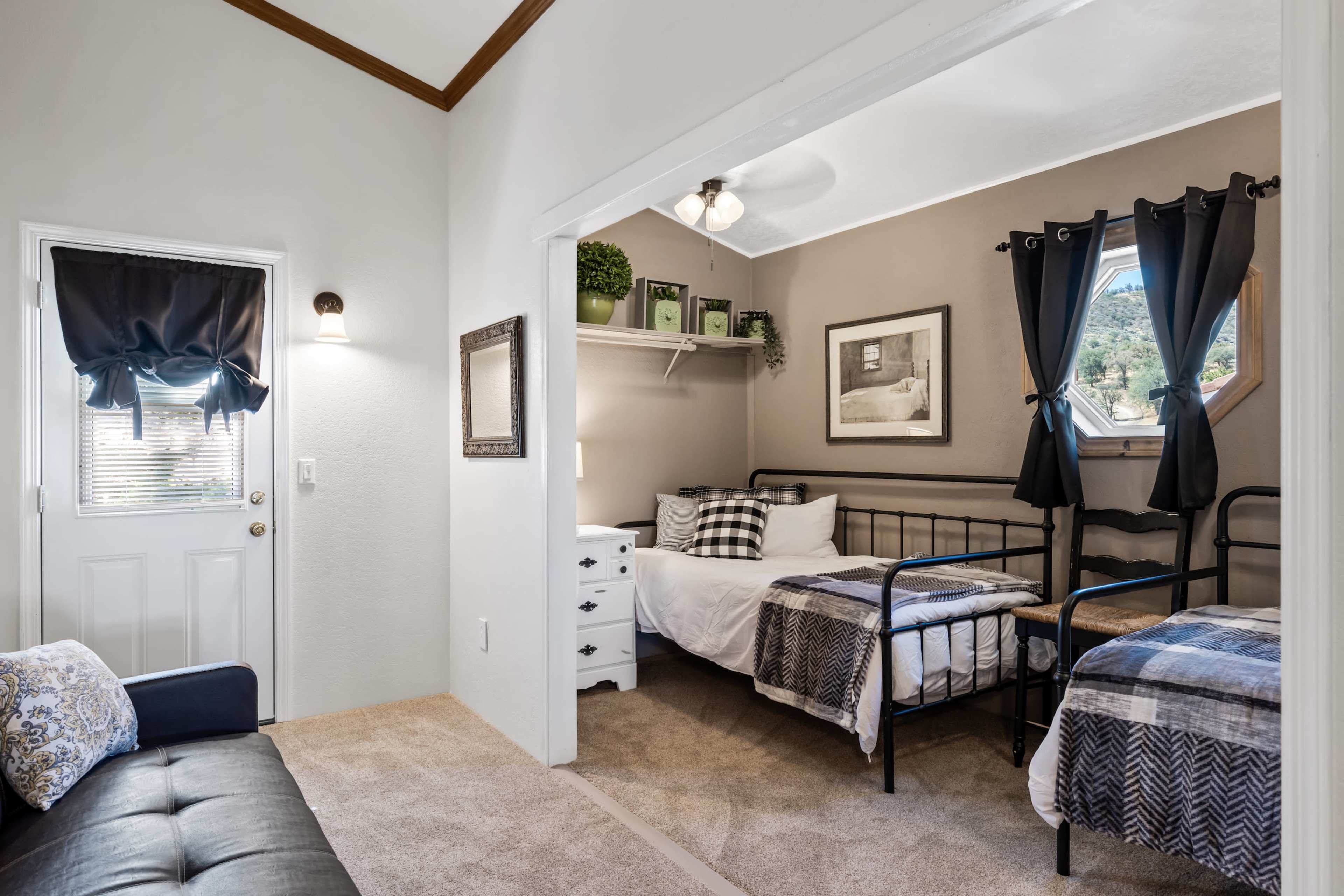 A small room featuring two twin beds, a dresser, and a door leading outside, with decorative elements and natural light.