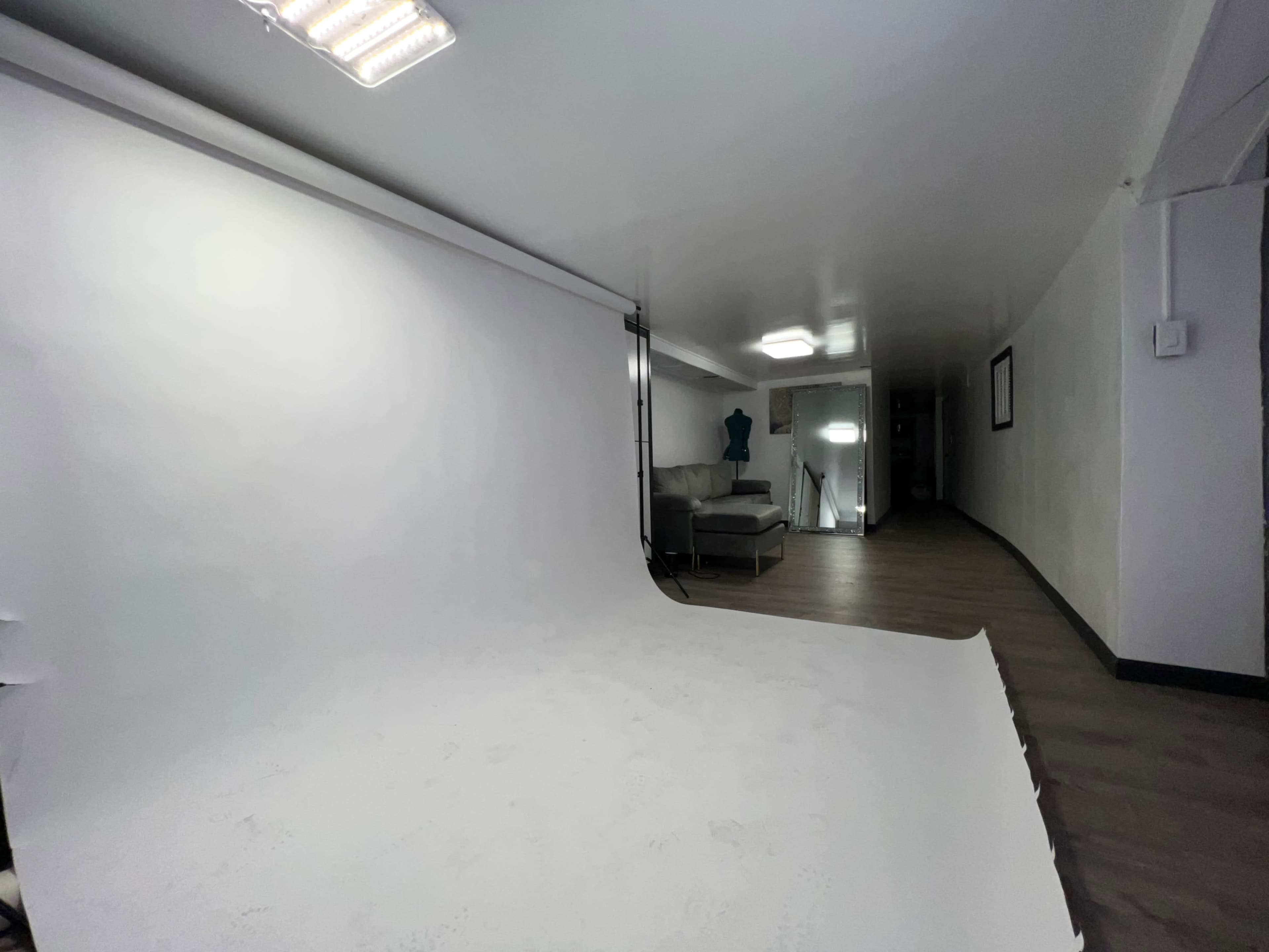 A photo studio with a white backdrop, a couch, and studio lights set up in a spacious room.