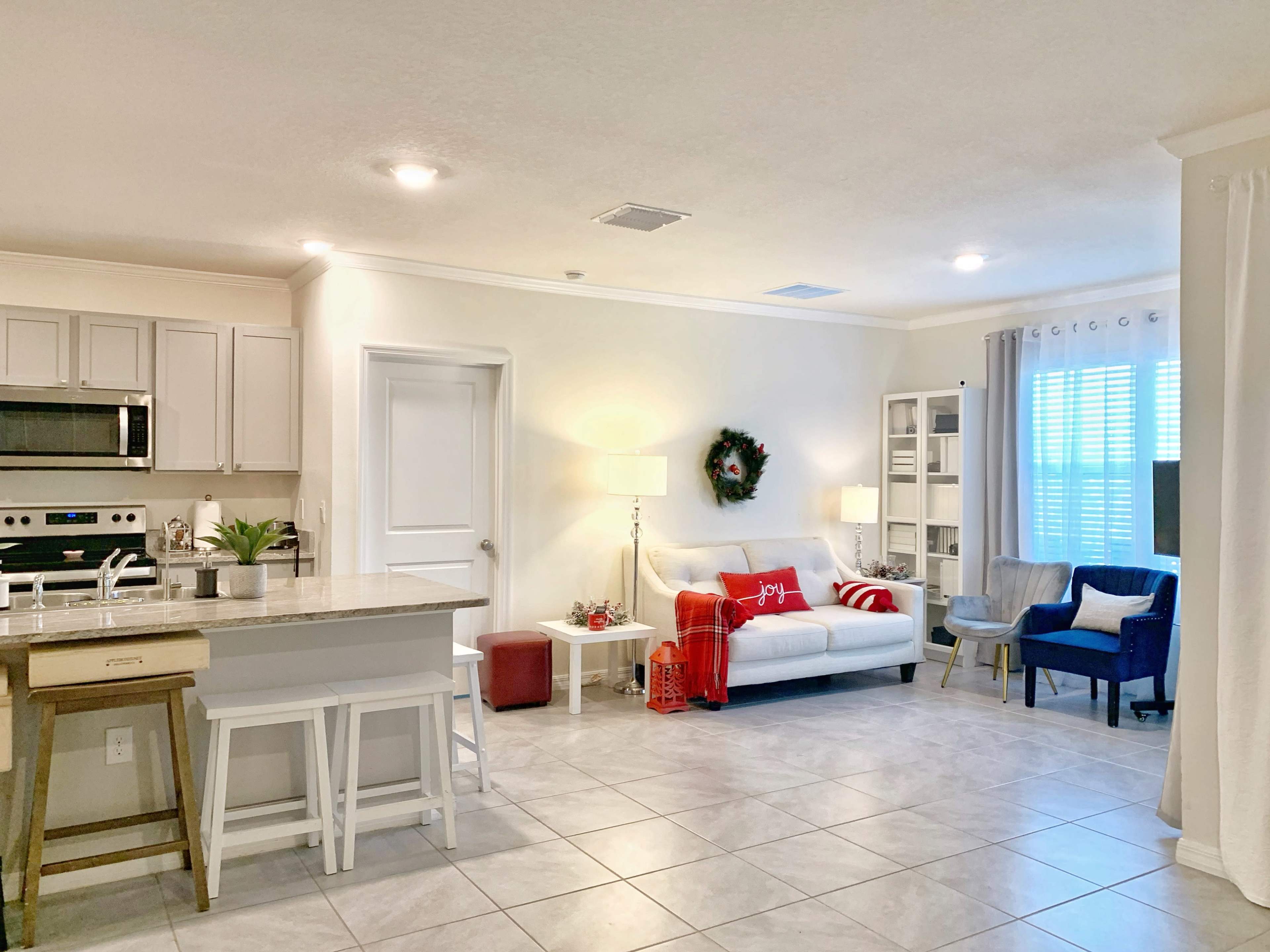 The image shows a modern living area and kitchen with light-colored cabinetry, a dining area, and a comfortable seating arrangement featuring a couch and armchairs.