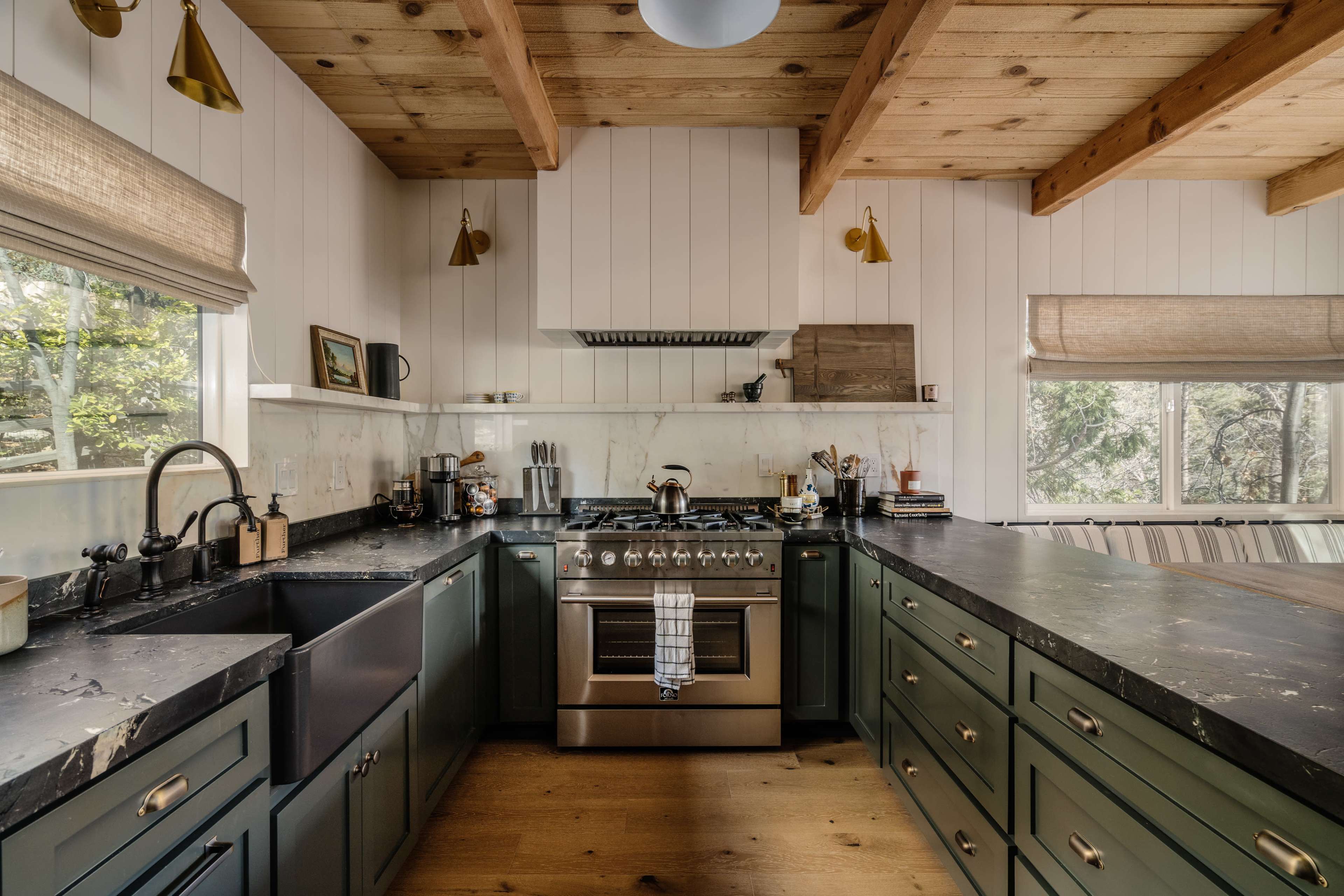 A modern kitchen with dark green cabinetry, a stainless steel stove, and wooden beams overhead.