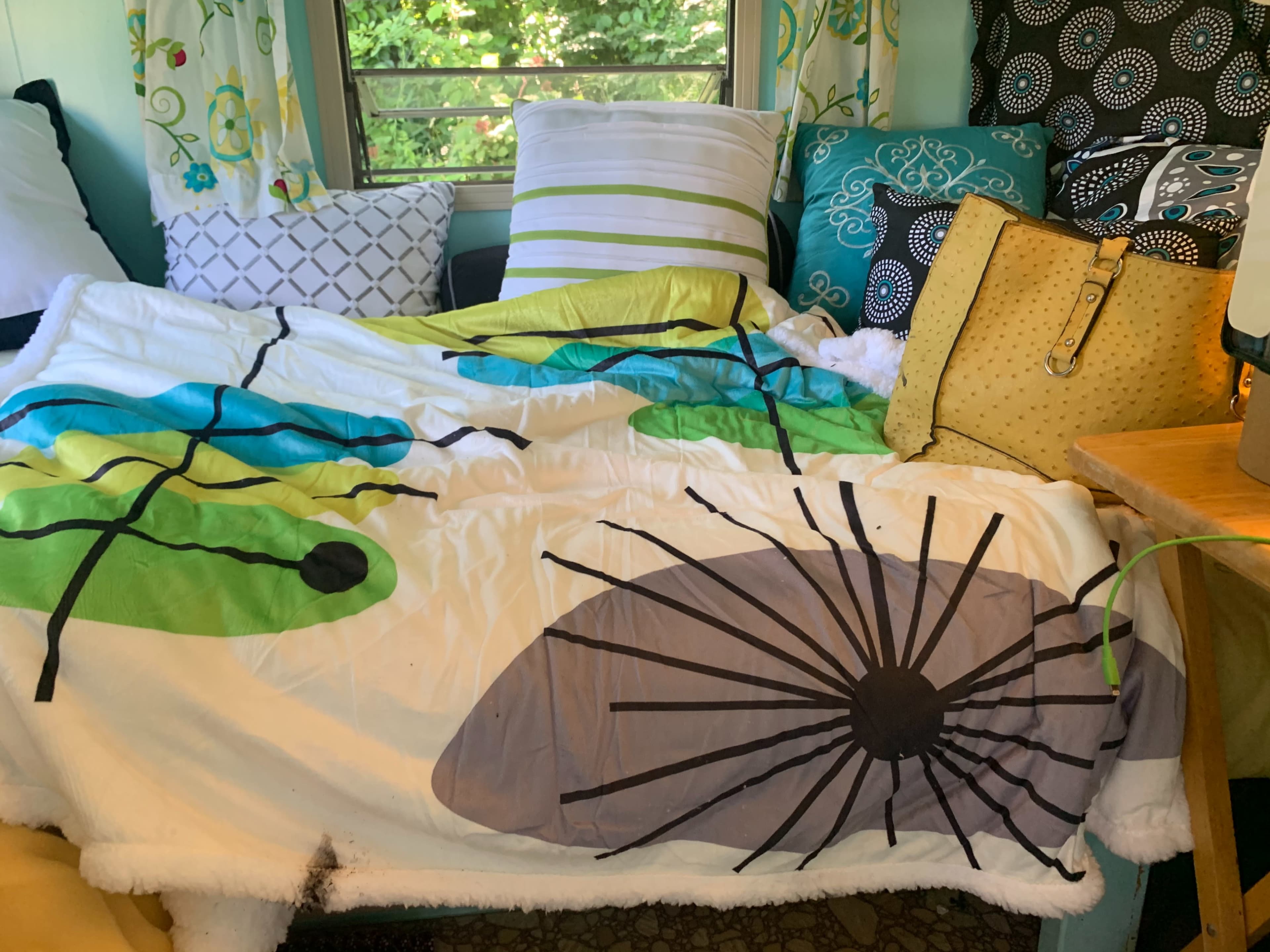 A colorful bedding spread with leaf patterns covers a couch surrounded by decorative pillows and a yellow bag.