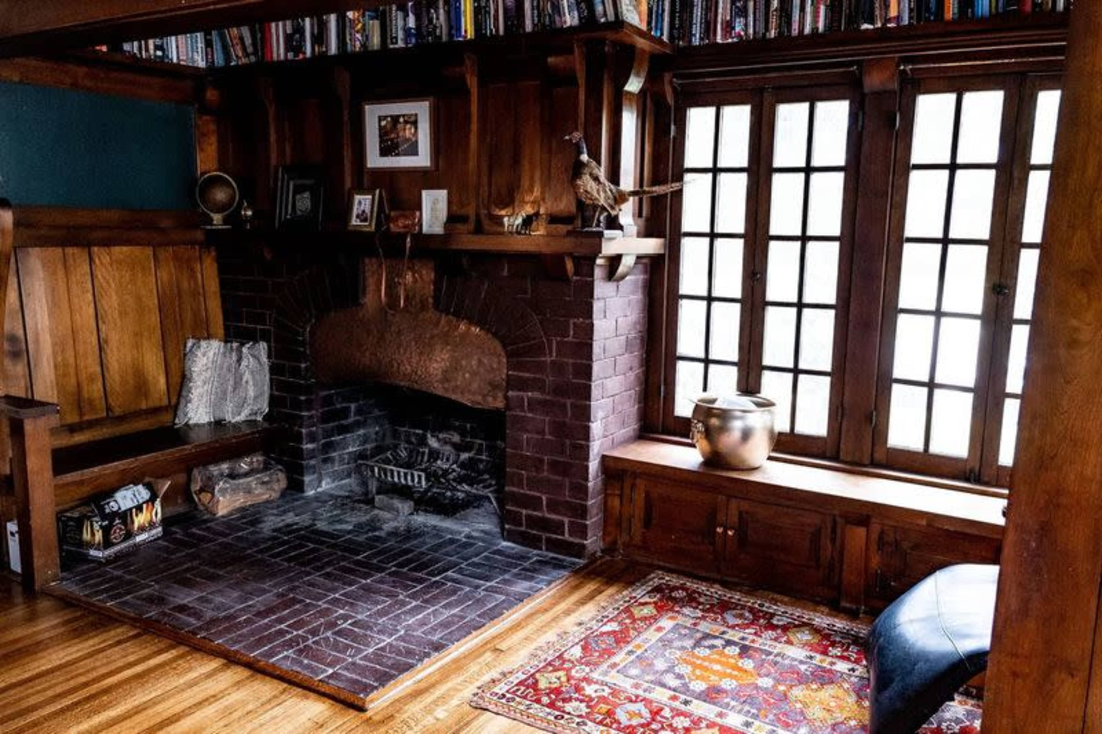 A cozy room with wooden walls, a fireplace, a built-in bench, a large window, and a patterned rug on the hardwood floor.