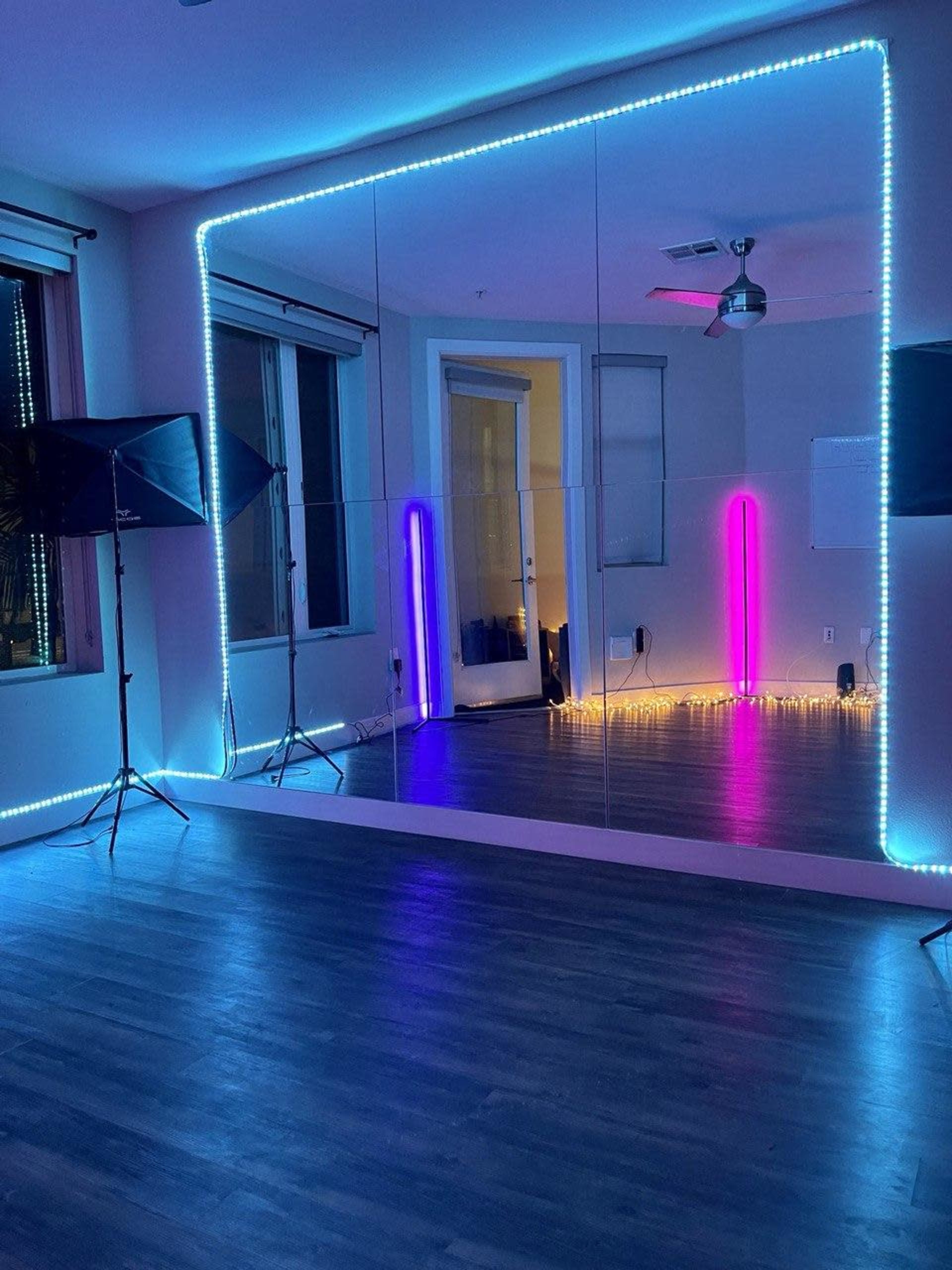 The image shows a room with mirrored walls illuminated by blue and purple LED lights, along with some string lights along the floor.