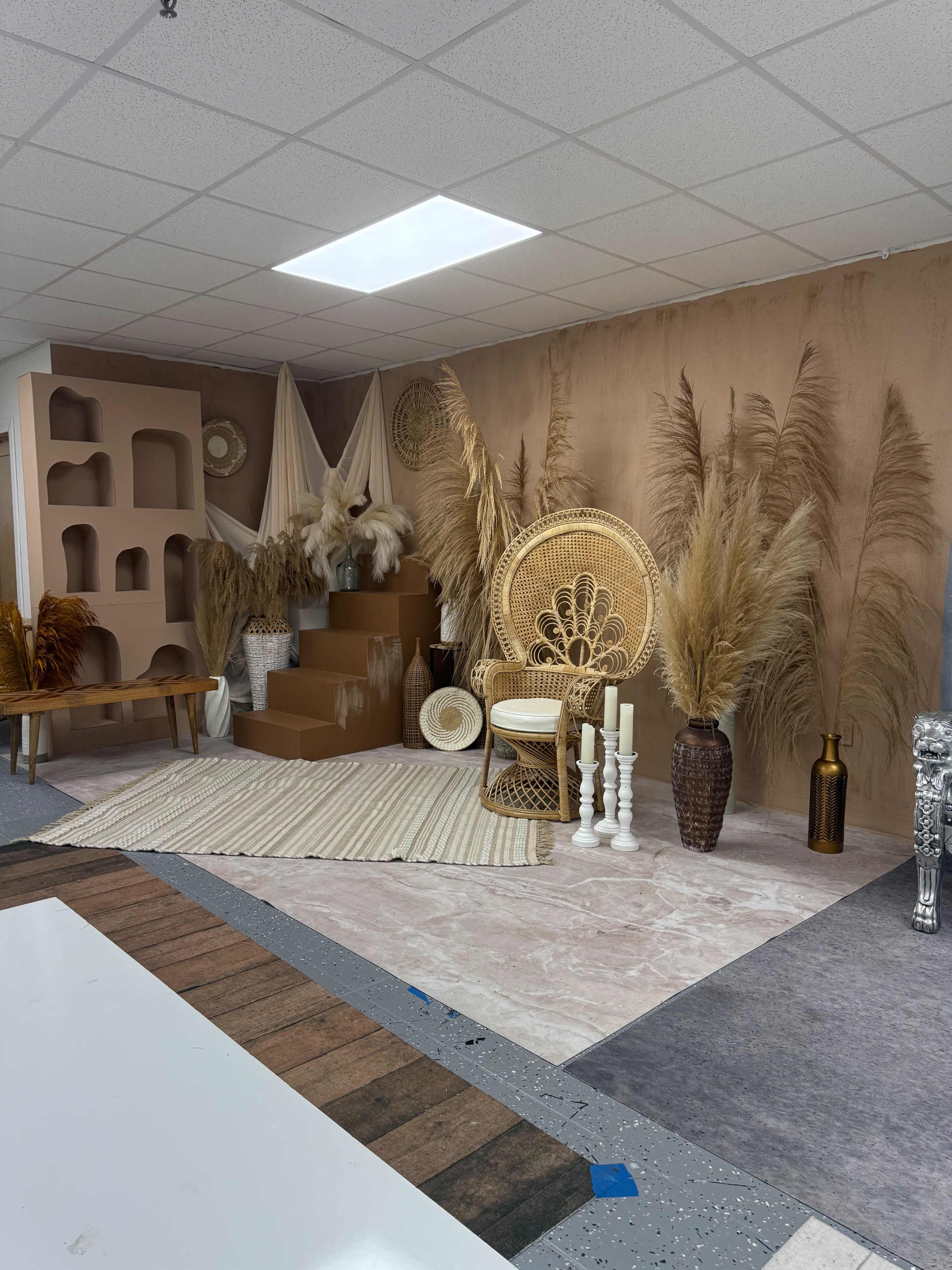 The image features a decorated studio space with a textured wall, a staircase adorned with dried plants, and various decorative items including a large wicker chair and candles.