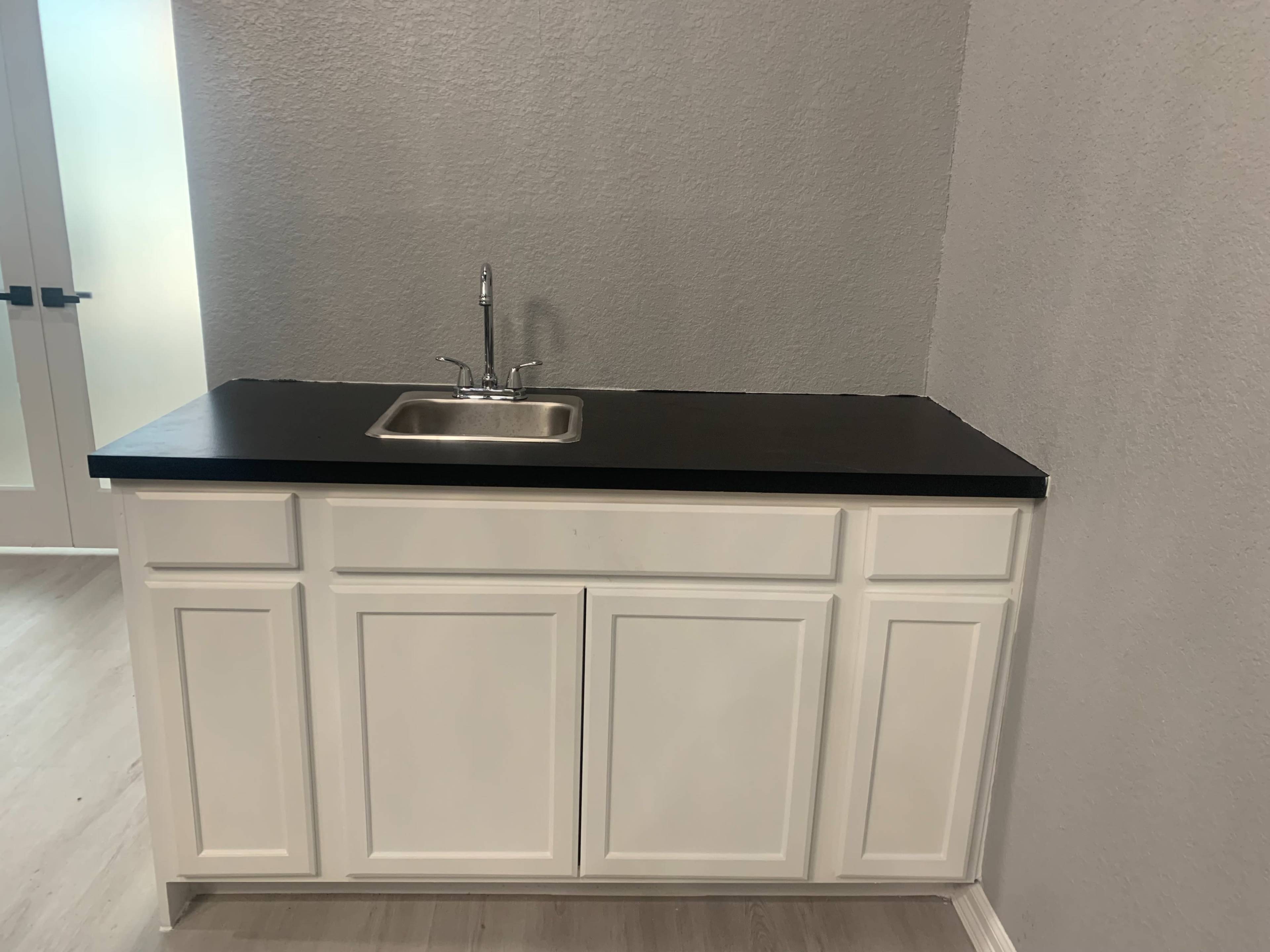 A white cabinet with a black countertop and a stainless steel sink in a room with gray walls.