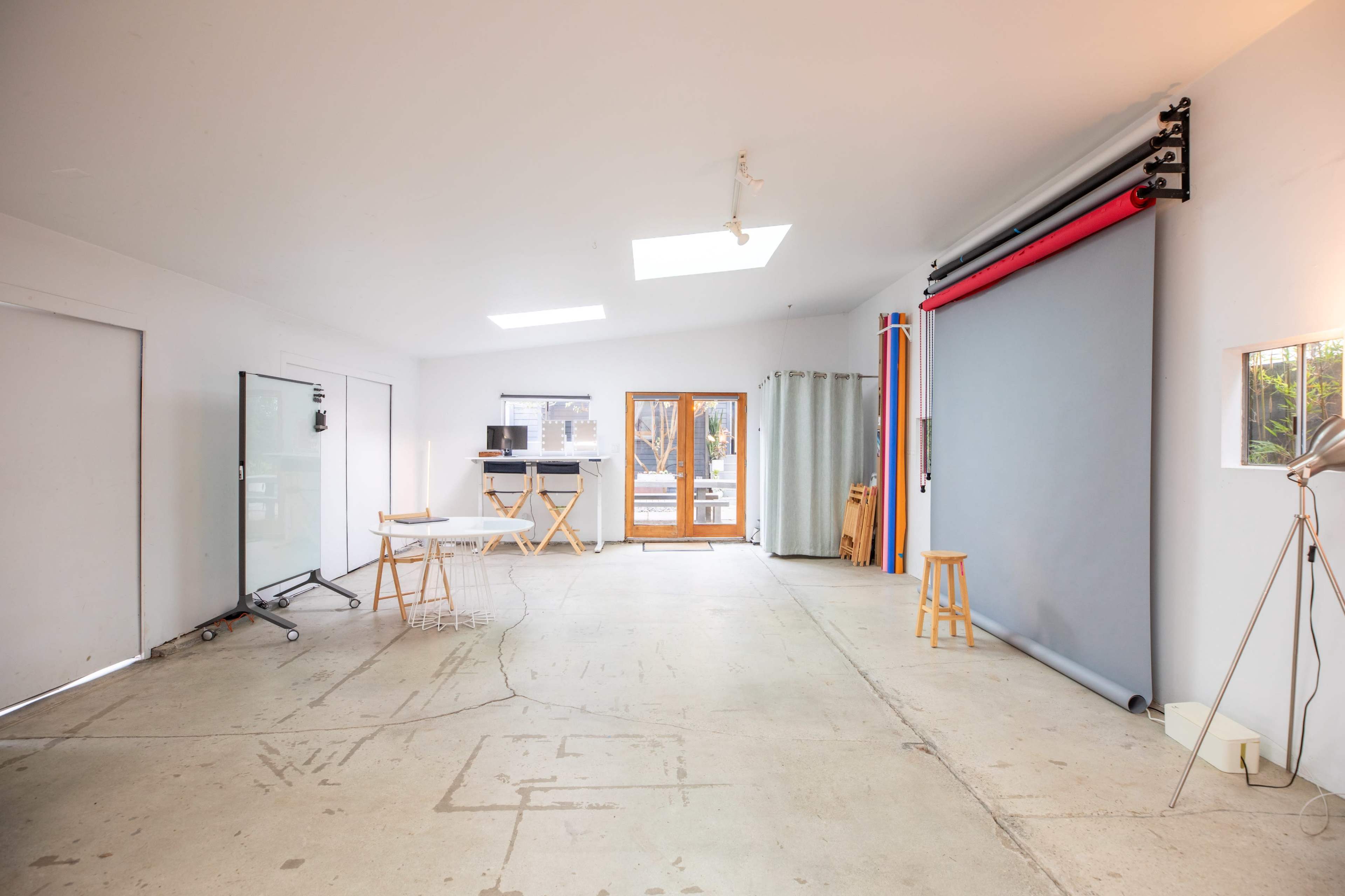A spacious, well-lit studio interior with a concrete floor, a backdrop setup, and various furniture including stools and tables.