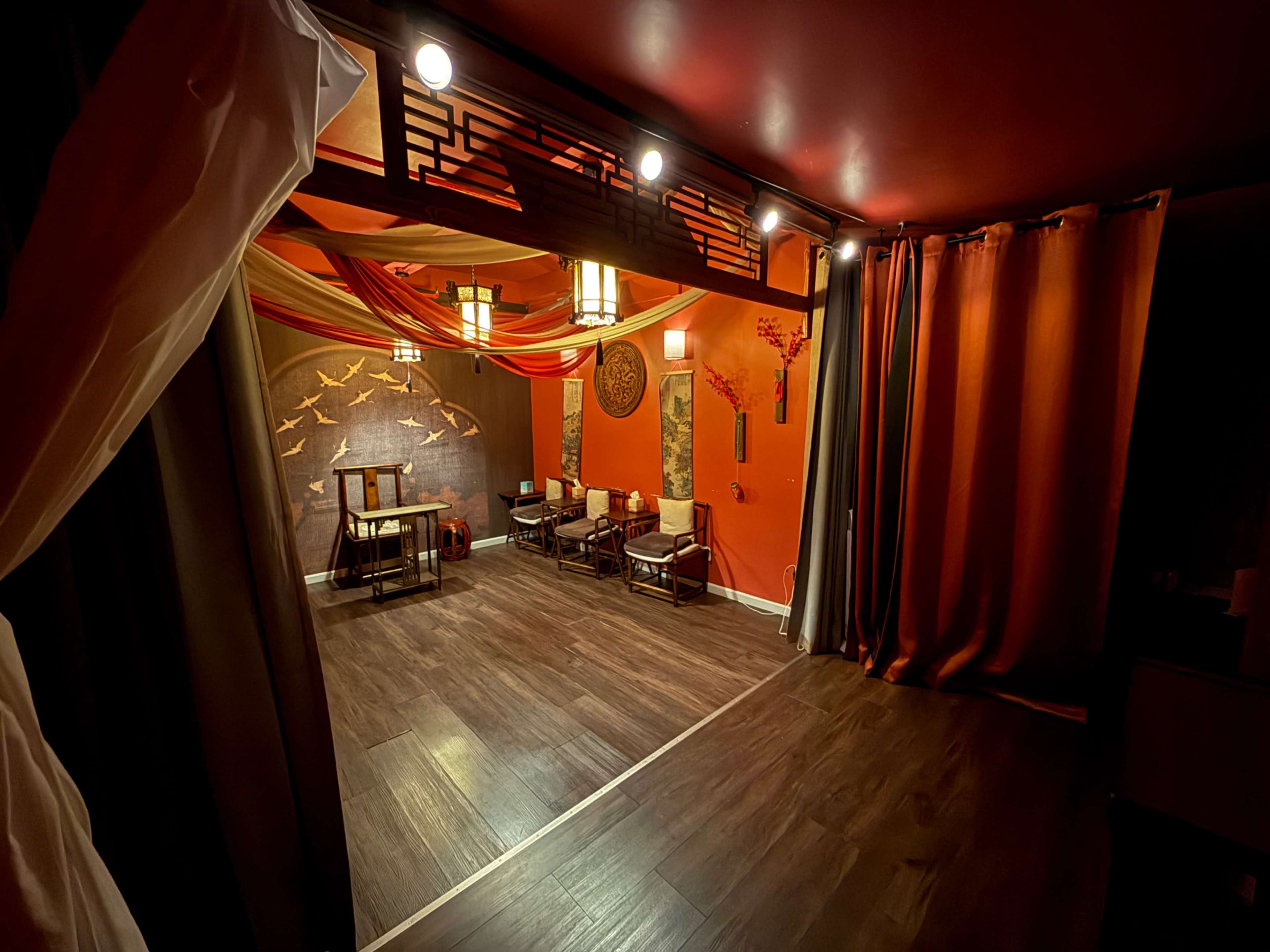 The image shows a cozy, well-decorated room with red walls, ambient lighting, and seating arranged around a small table.