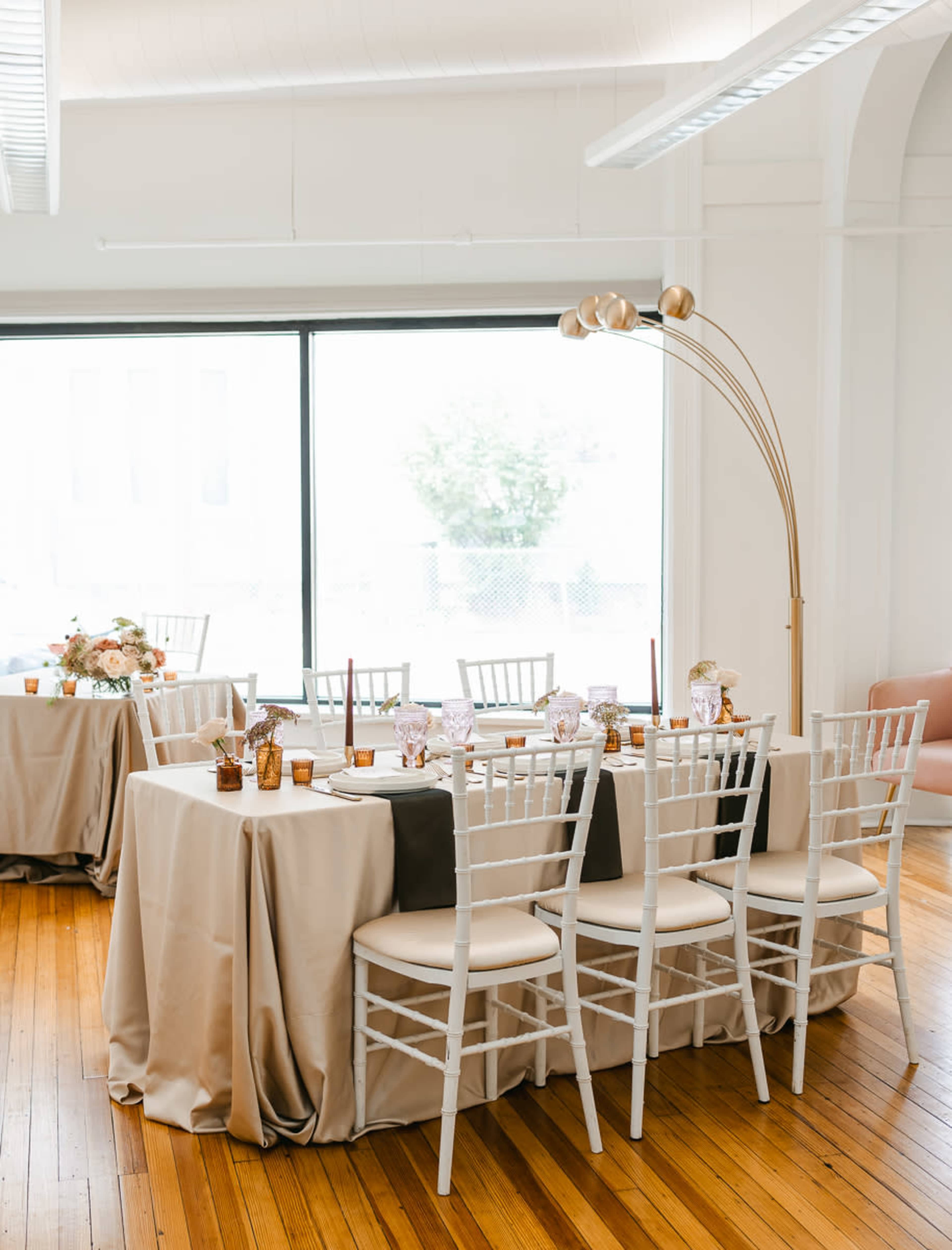 A well-decorated event space features elegantly set tables with light-colored tablecloths and decorative centerpieces.