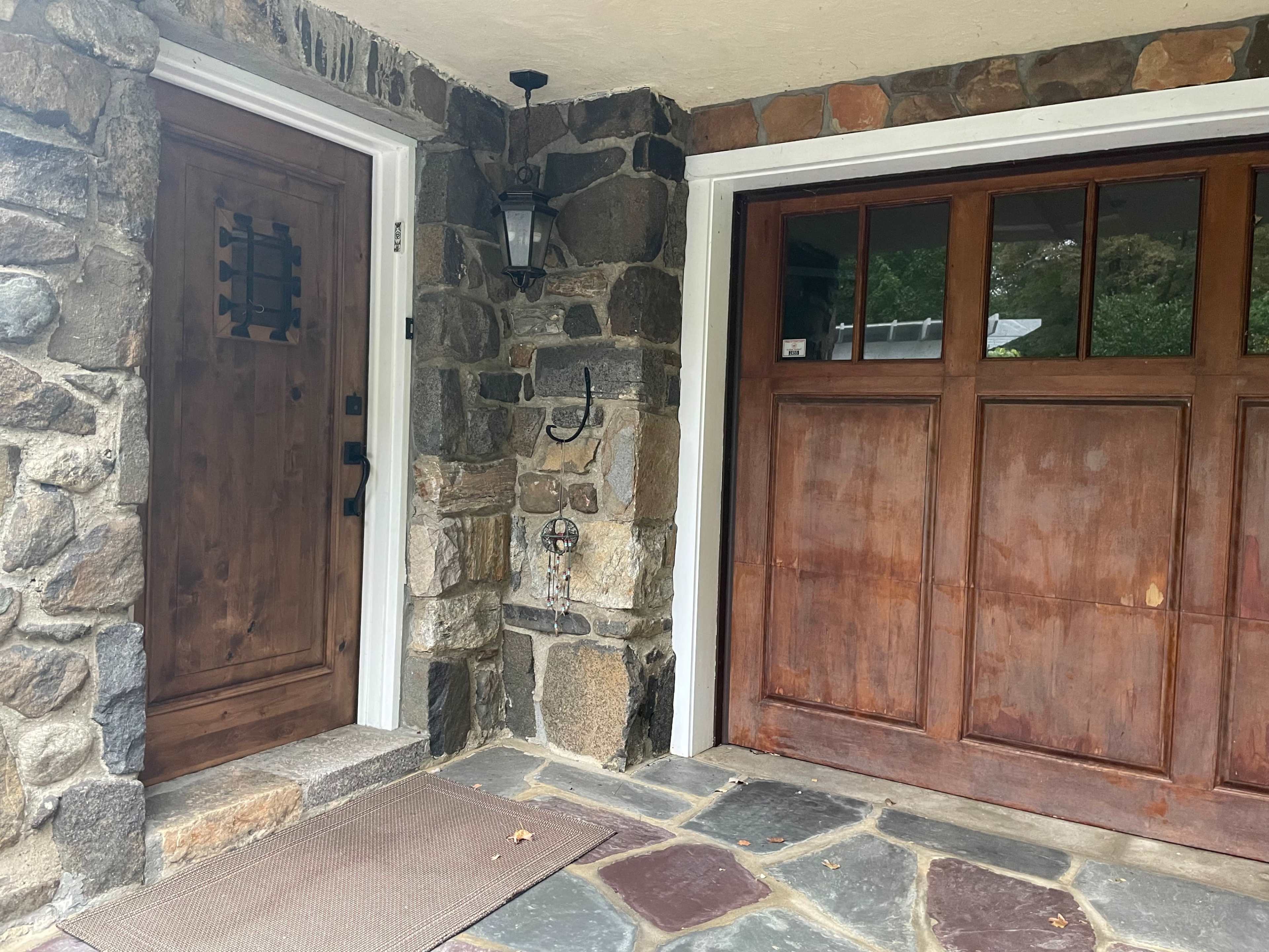A stone wall with a wooden door on the left and a wooden garage door on the right, both set under a covered entryway.