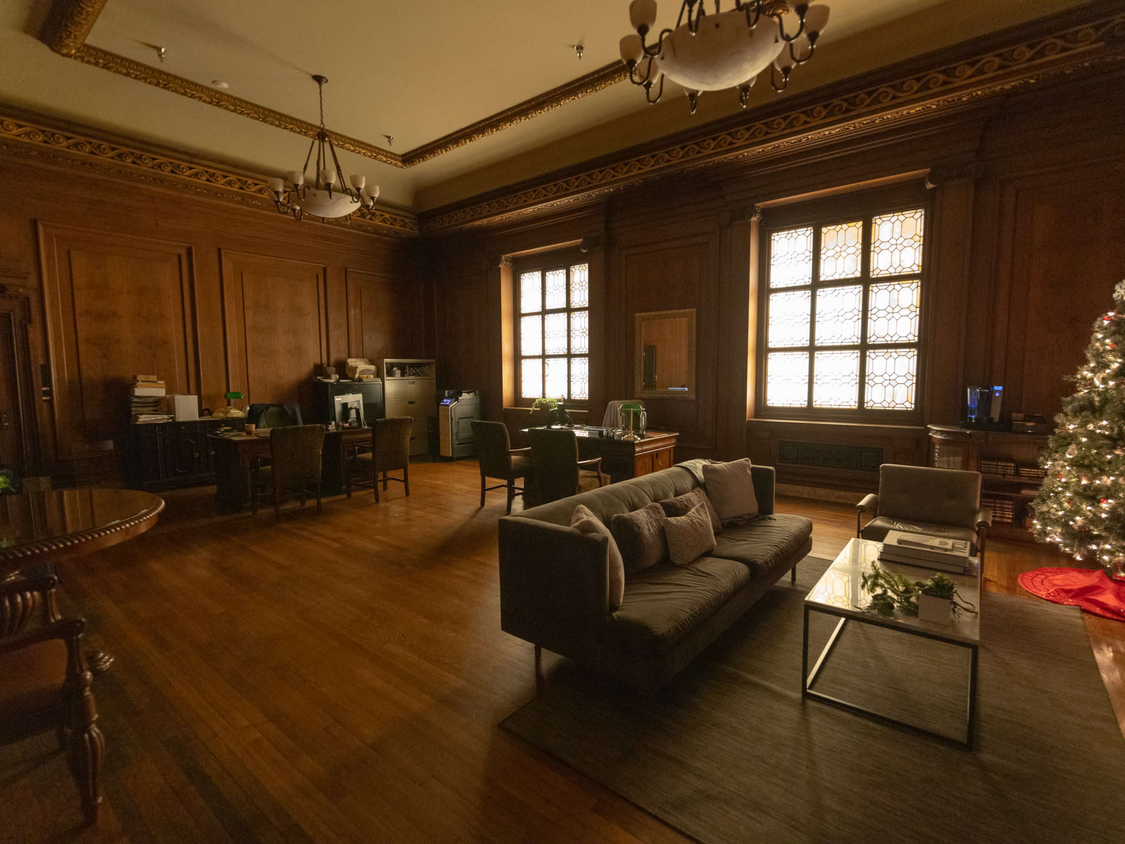 The image depicts a wooden-paneled room with a sofa, a coffee table, a Christmas tree, and workstations along the walls.