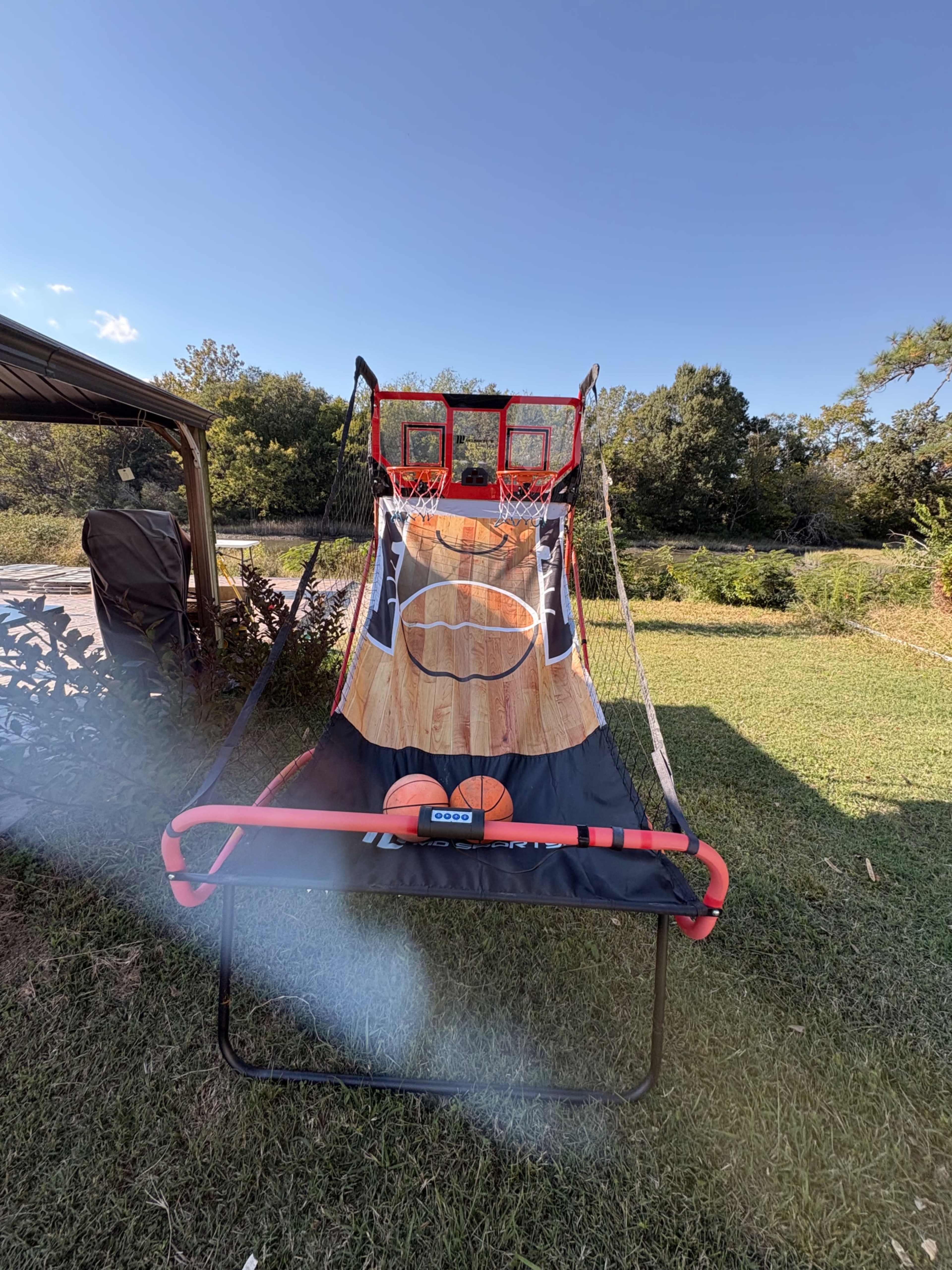 A basketball shooting game is set up outdoors on a grassy area, featuring two hoops and a vibrant design.