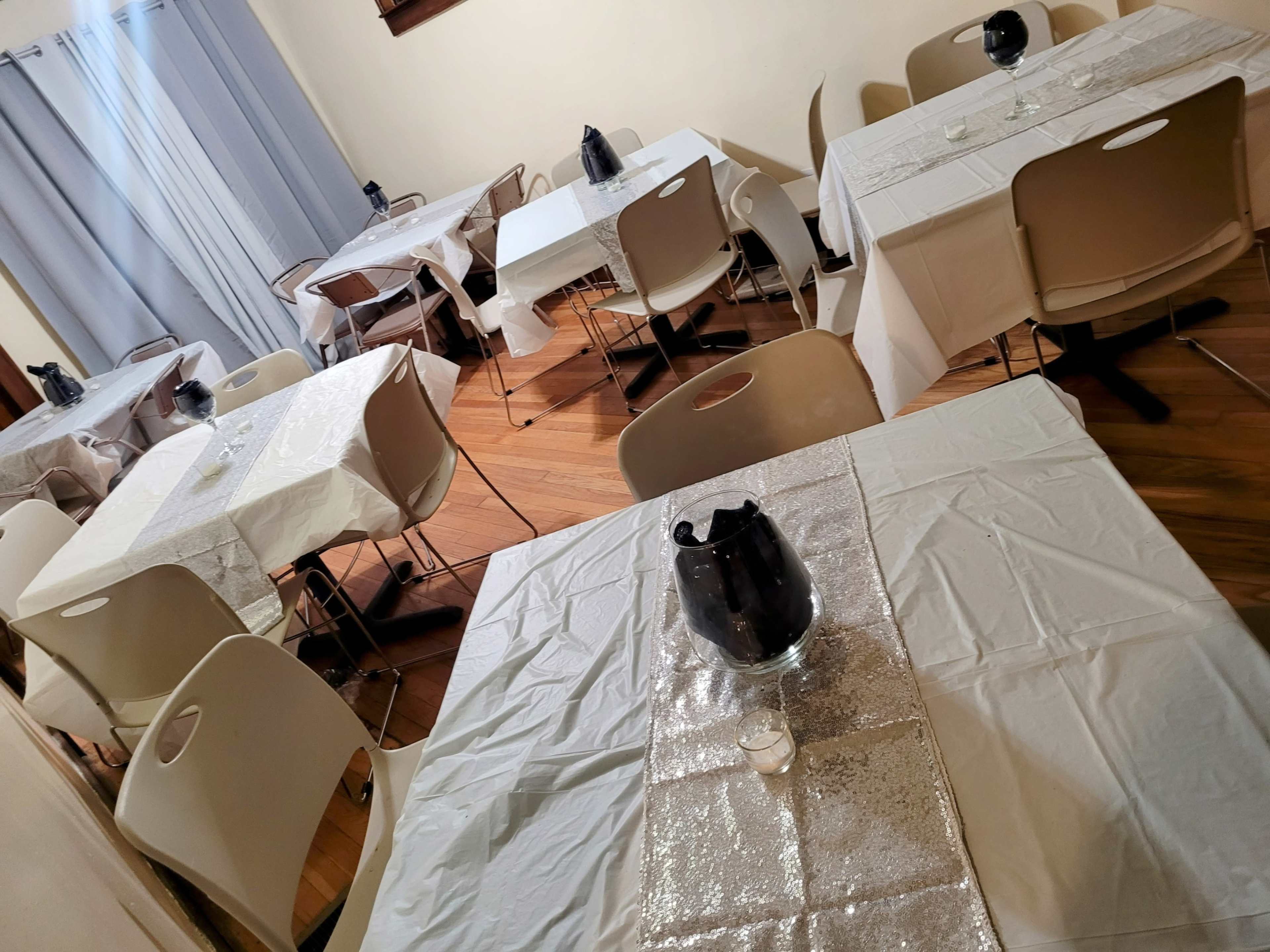The image depicts a dining area with several covered tables arranged neatly, each featuring a water pitcher and a candle.