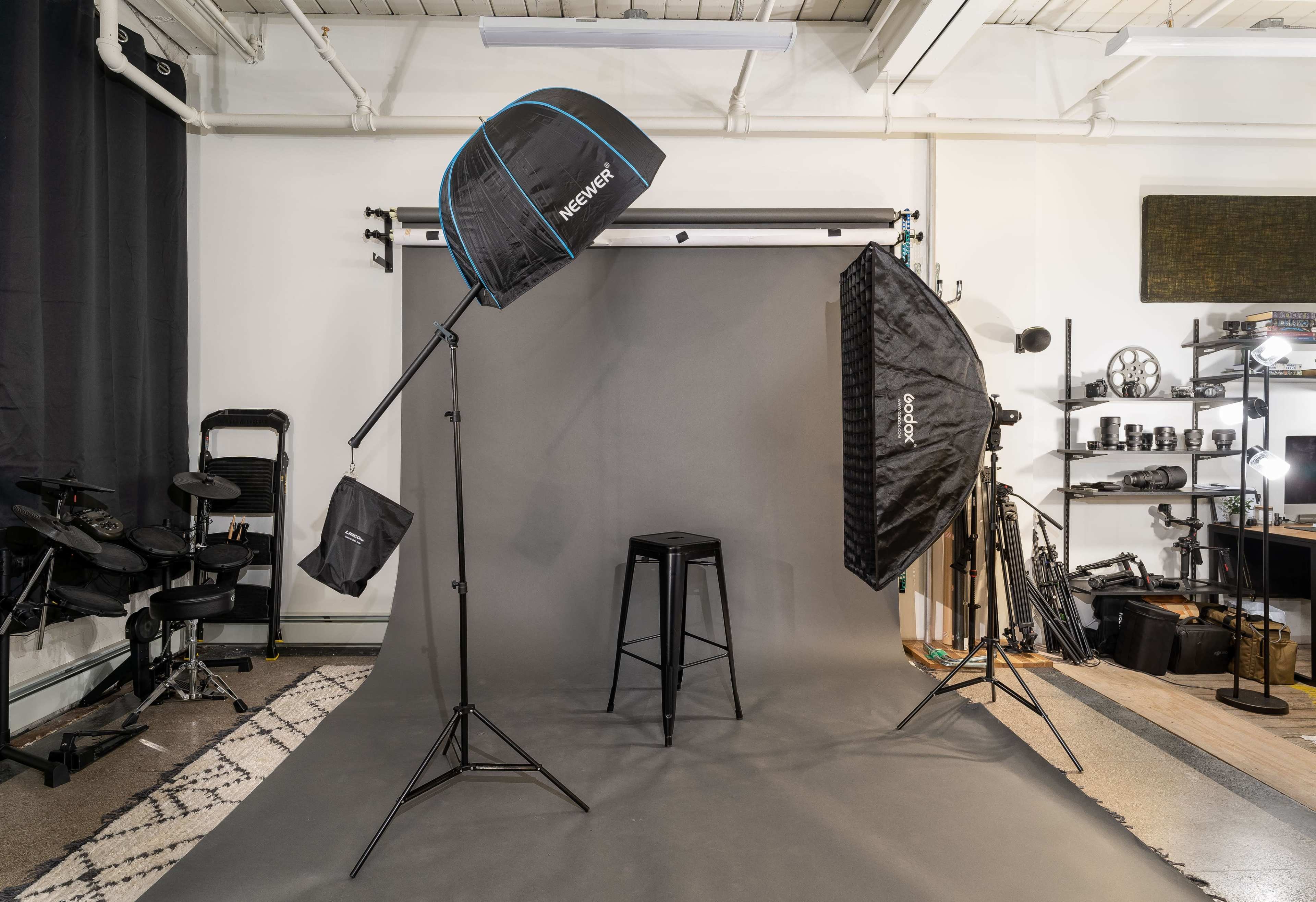 A photography studio setup with lighting equipment, a grey backdrop, and a stool positioned in the center.
