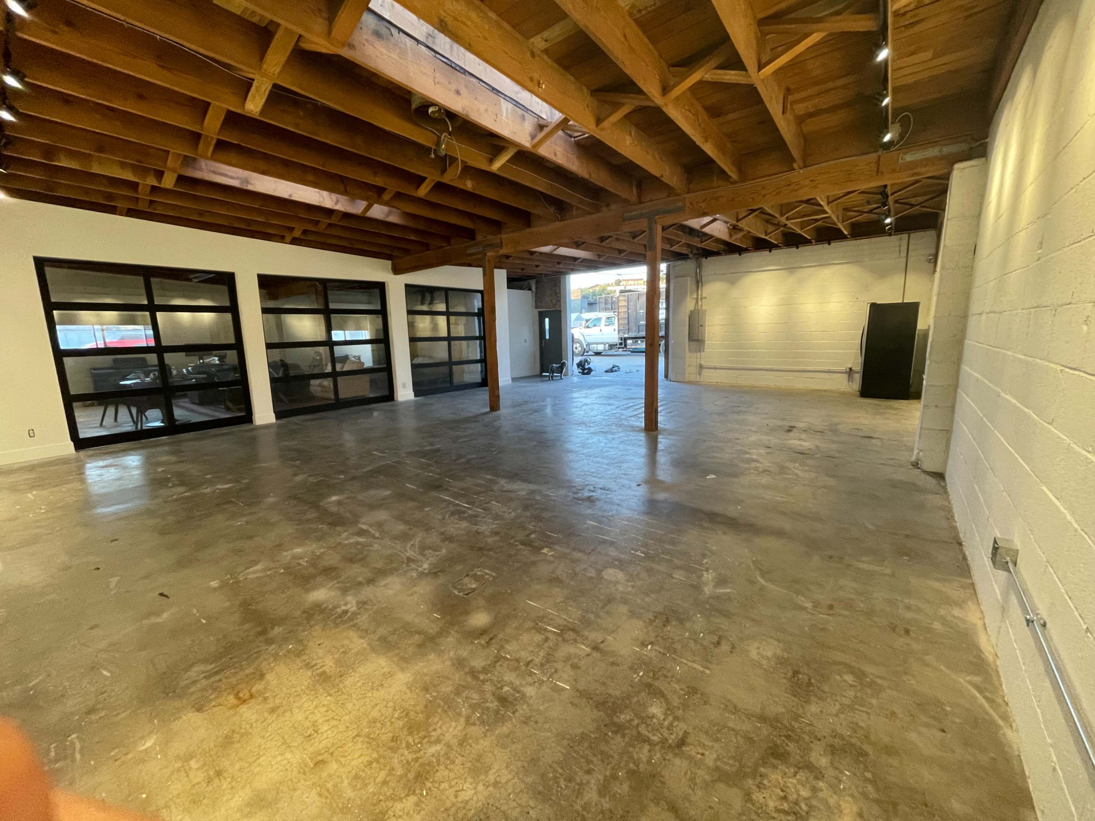 An empty industrial-style space with exposed wooden beams and concrete flooring.