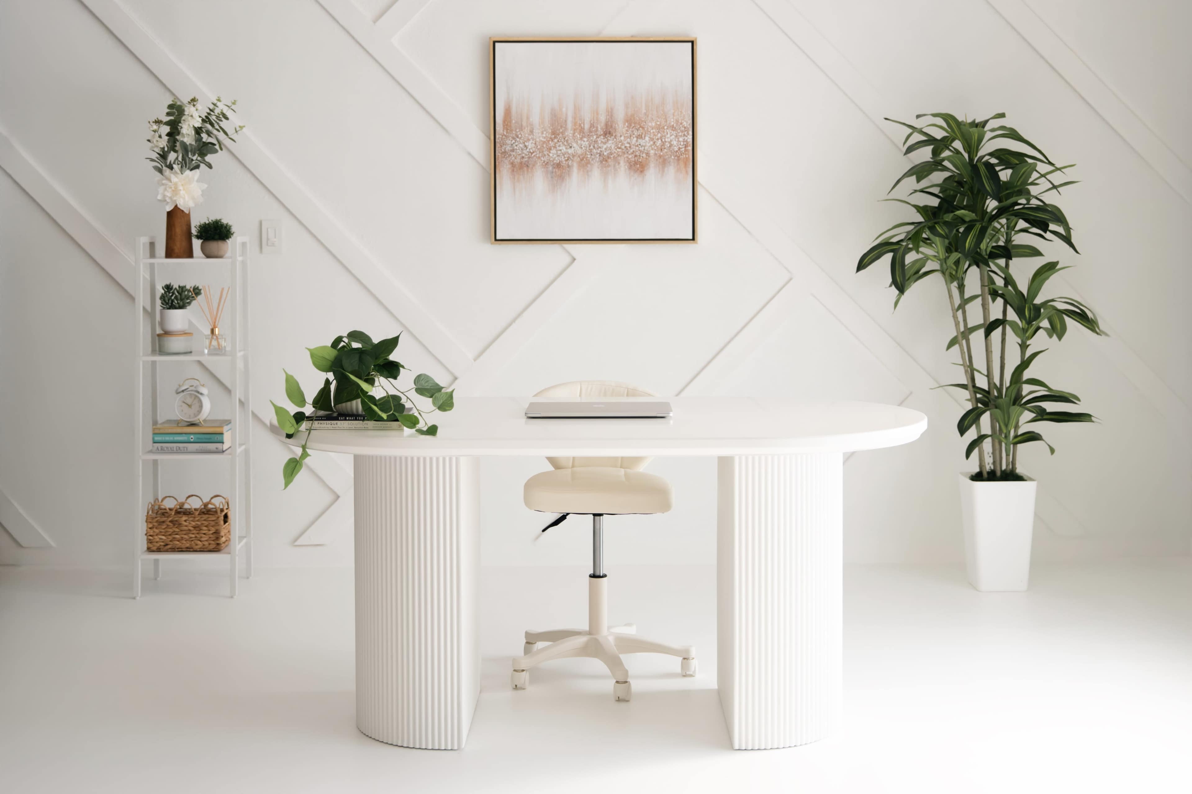A modern office space features a white oval desk, a rolling chair, a plant, and decorative plants on a shelf against a geometric-patterned wall.