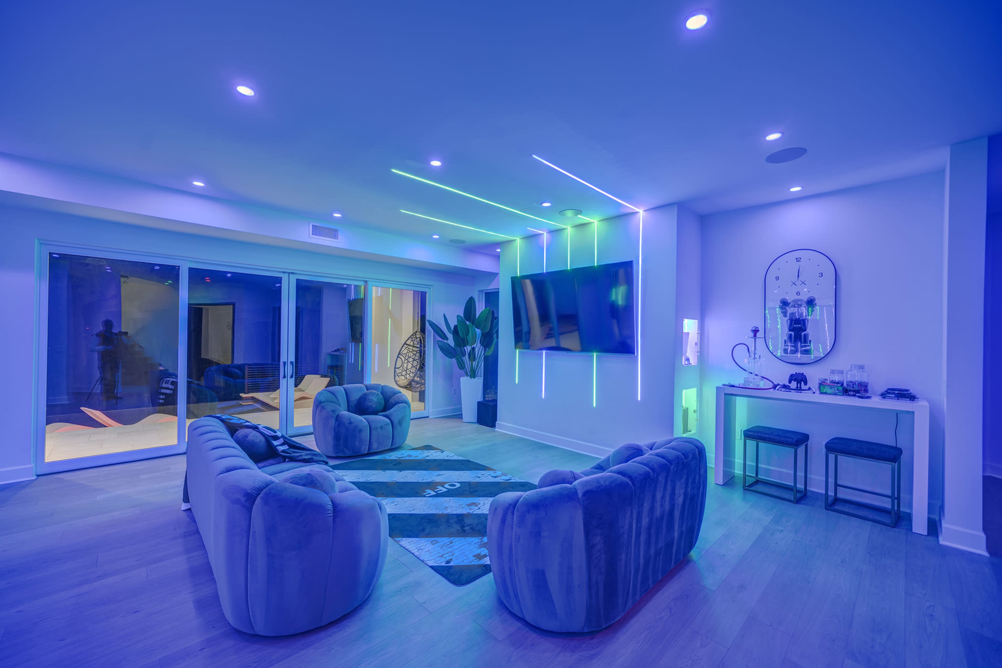 A modern living room features two plush sofas, a large wall-mounted TV, and ambient LED lighting.