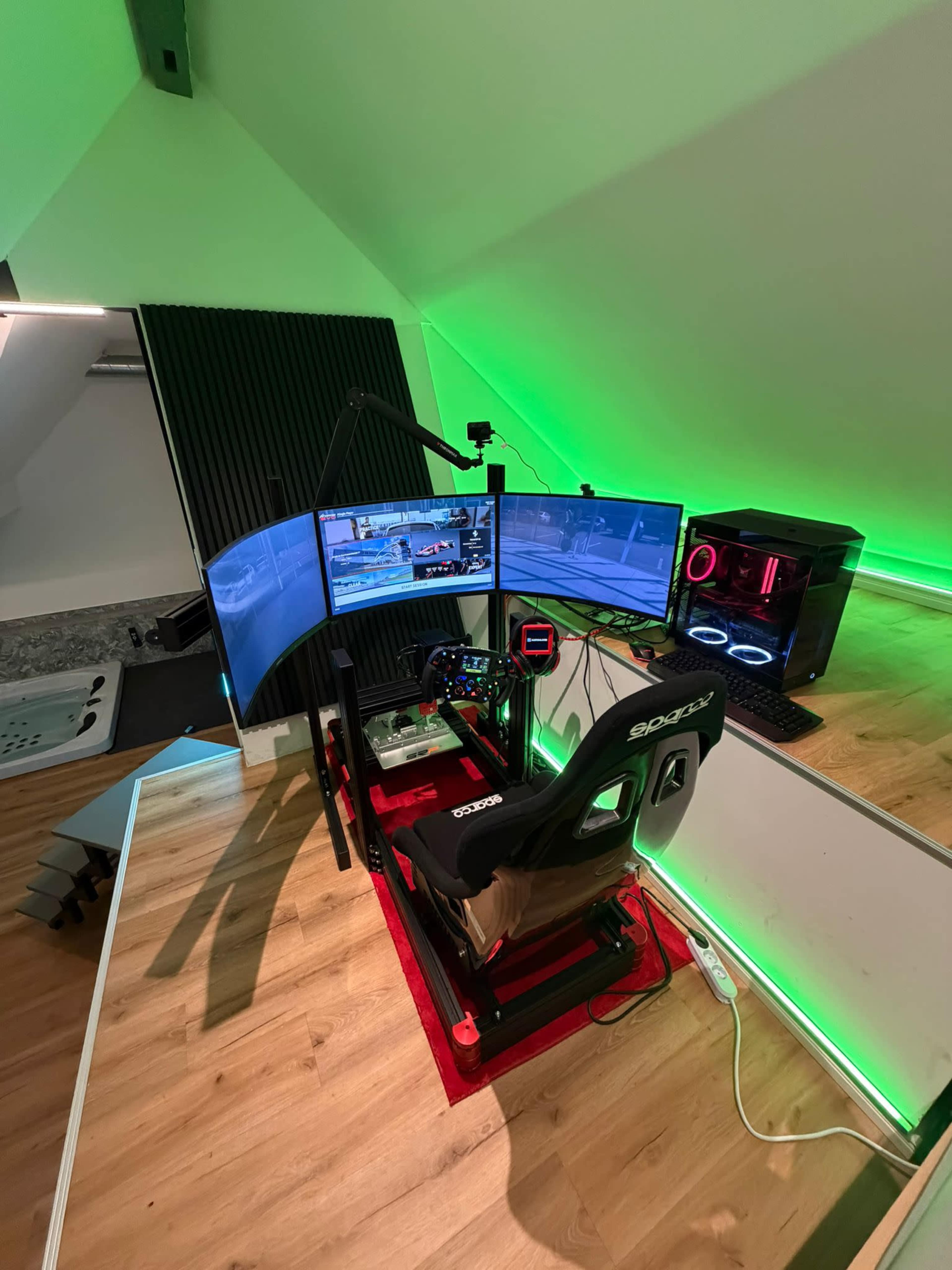 The image shows a gaming setup featuring three monitors arranged in a curved configuration, a racing simulator chair, and a desktop computer with RGB lighting, all set in a modern, brightly lit room.