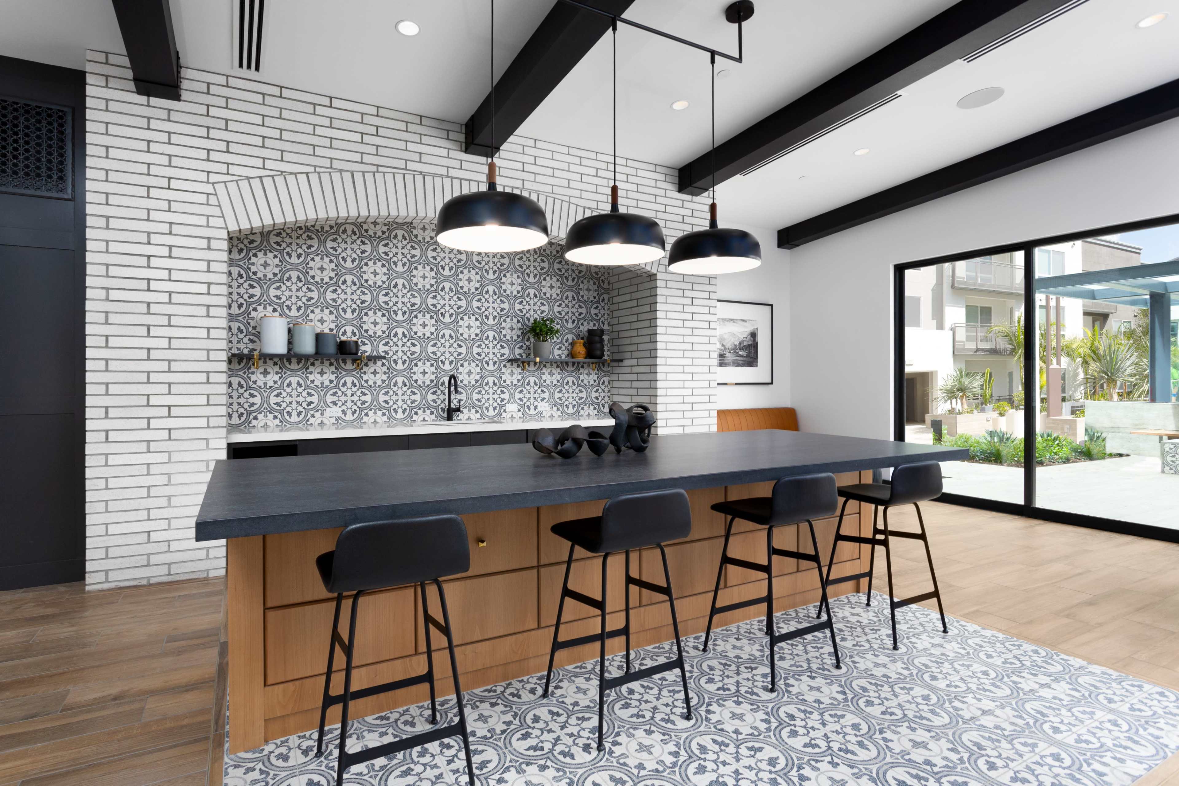 A modern kitchen features a large island with black bar stools, a patterned backsplash, and a sliding glass door that opens to an outdoor space.