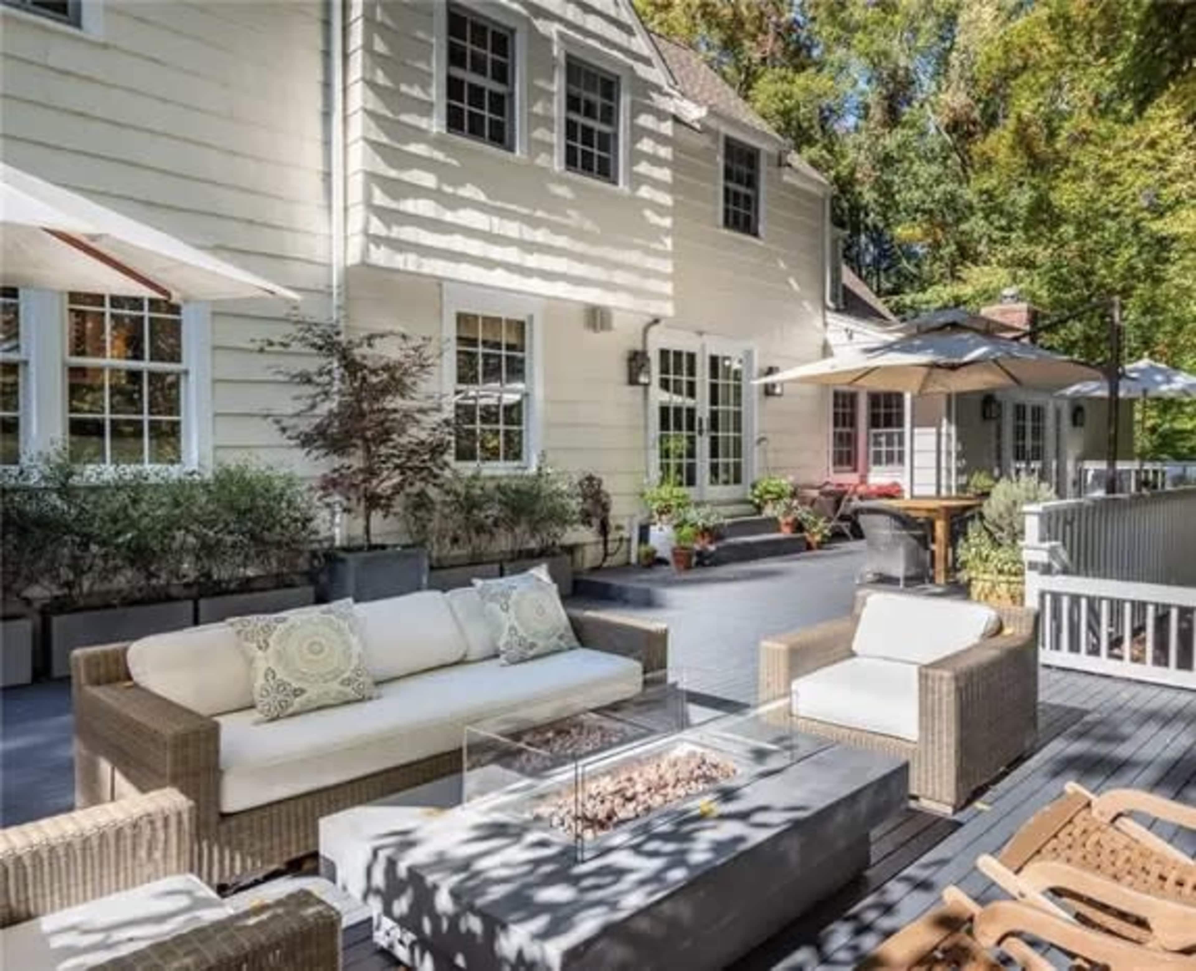 A spacious patio features a seating area with a fire pit, surrounded by plants and outdoor umbrellas.