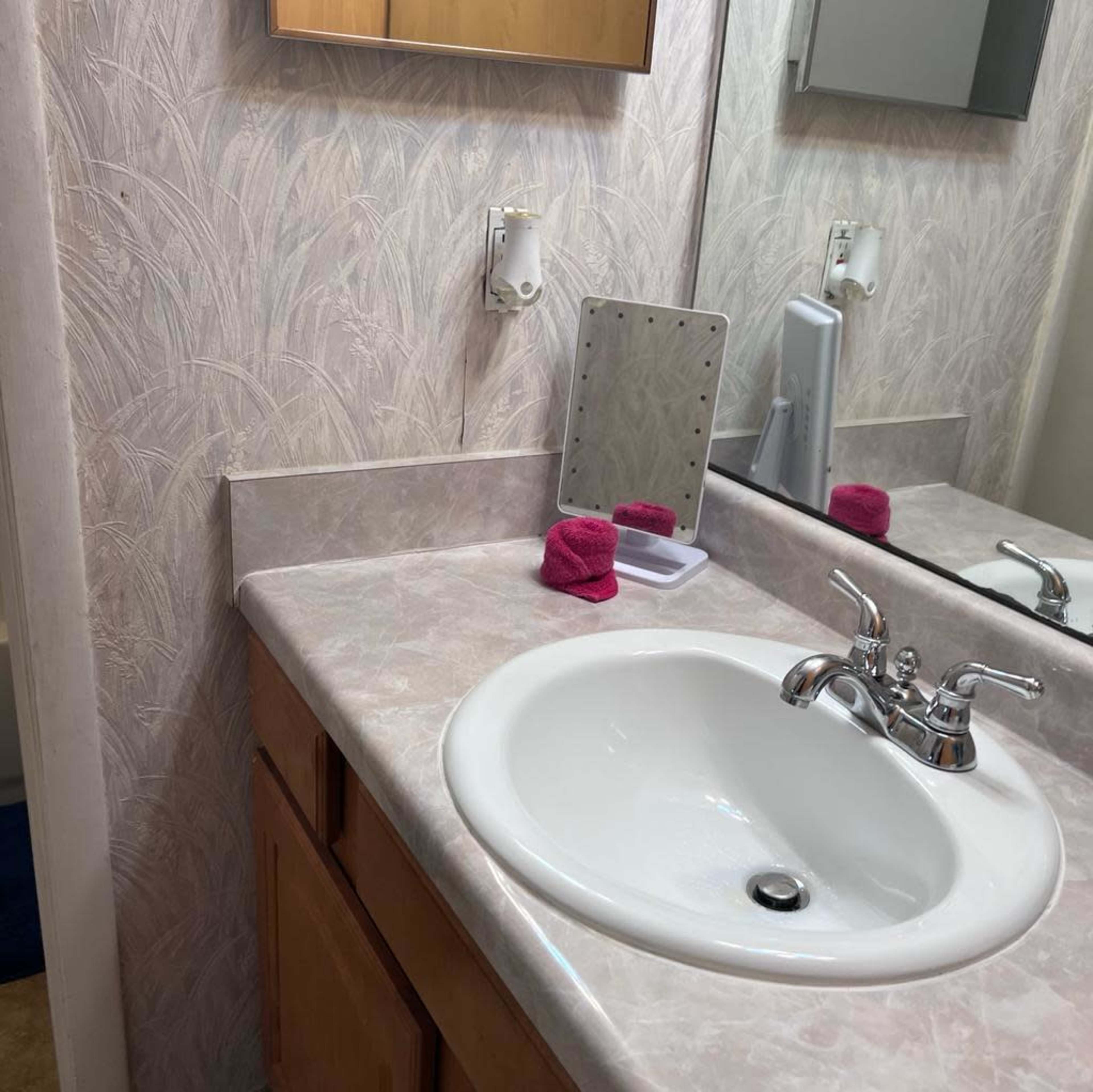 A bathroom sink with a marble-like countertop, a small mirror, and two pink towels on the surface.