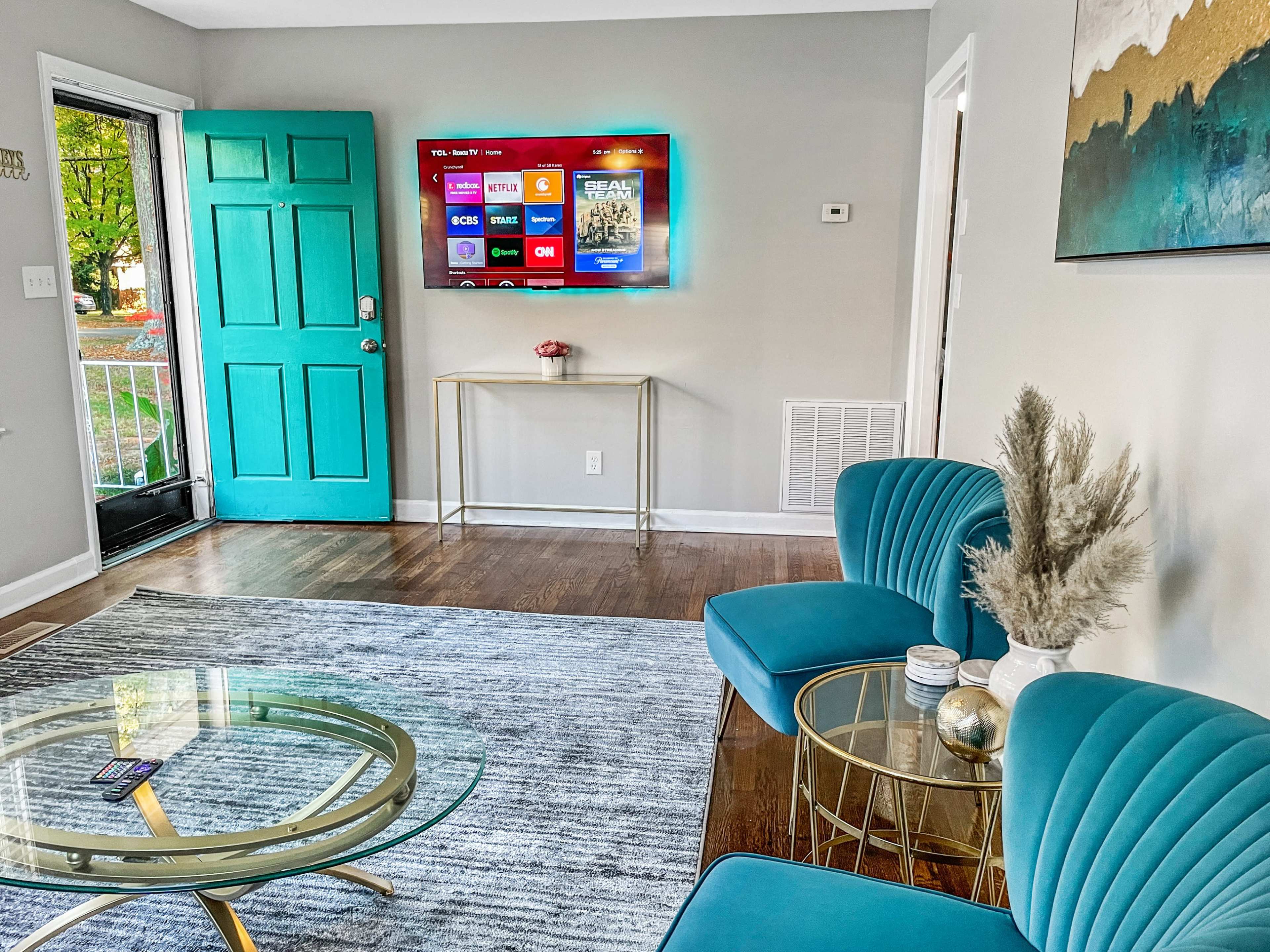 A bright living room features a teal door, modern furniture, and a wall-mounted TV displaying streaming options.