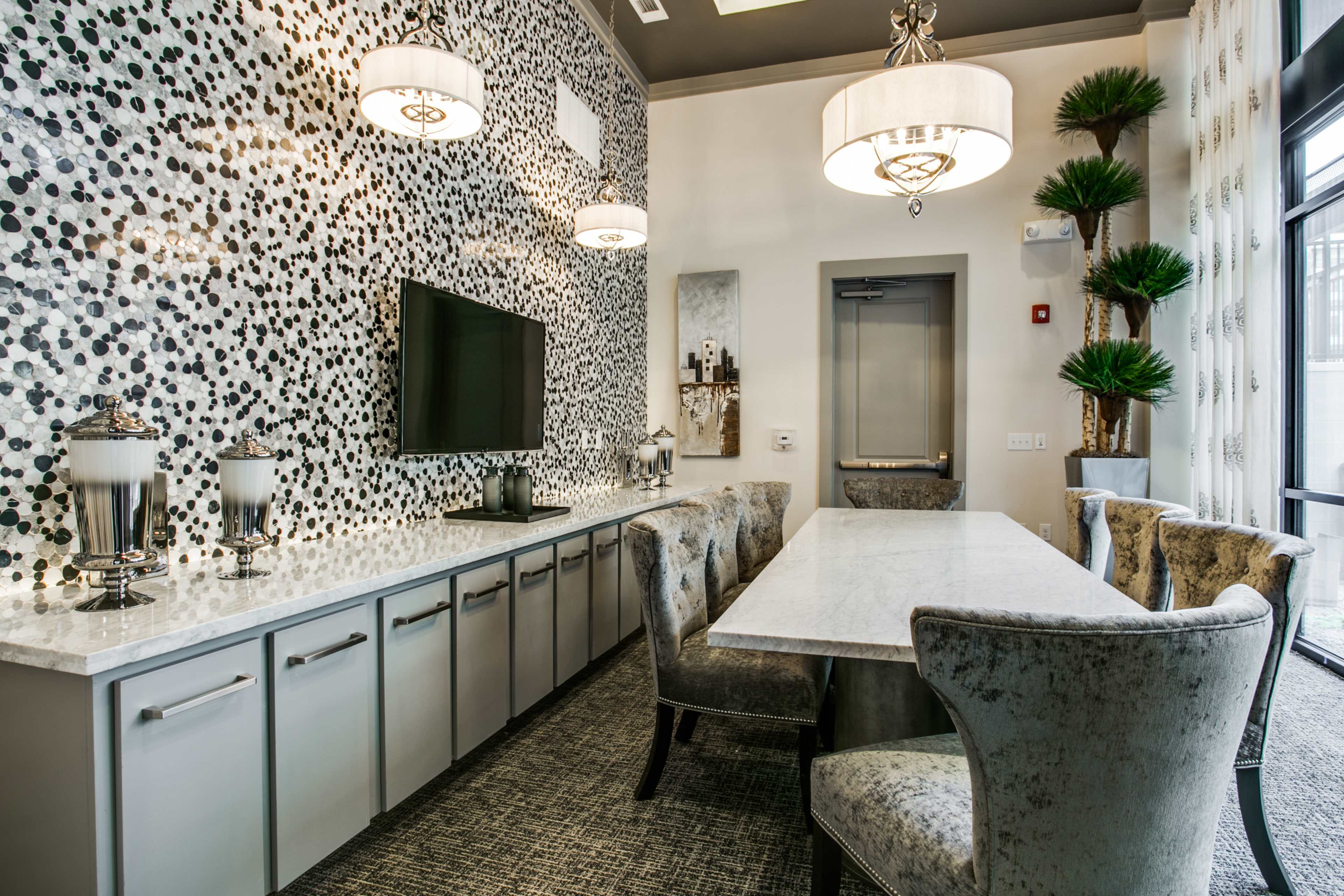 The image shows a modern dining room with a marble table surrounded by upholstered chairs, a wall decorated with a black and white polka dot pattern, and a television mounted on the wall.