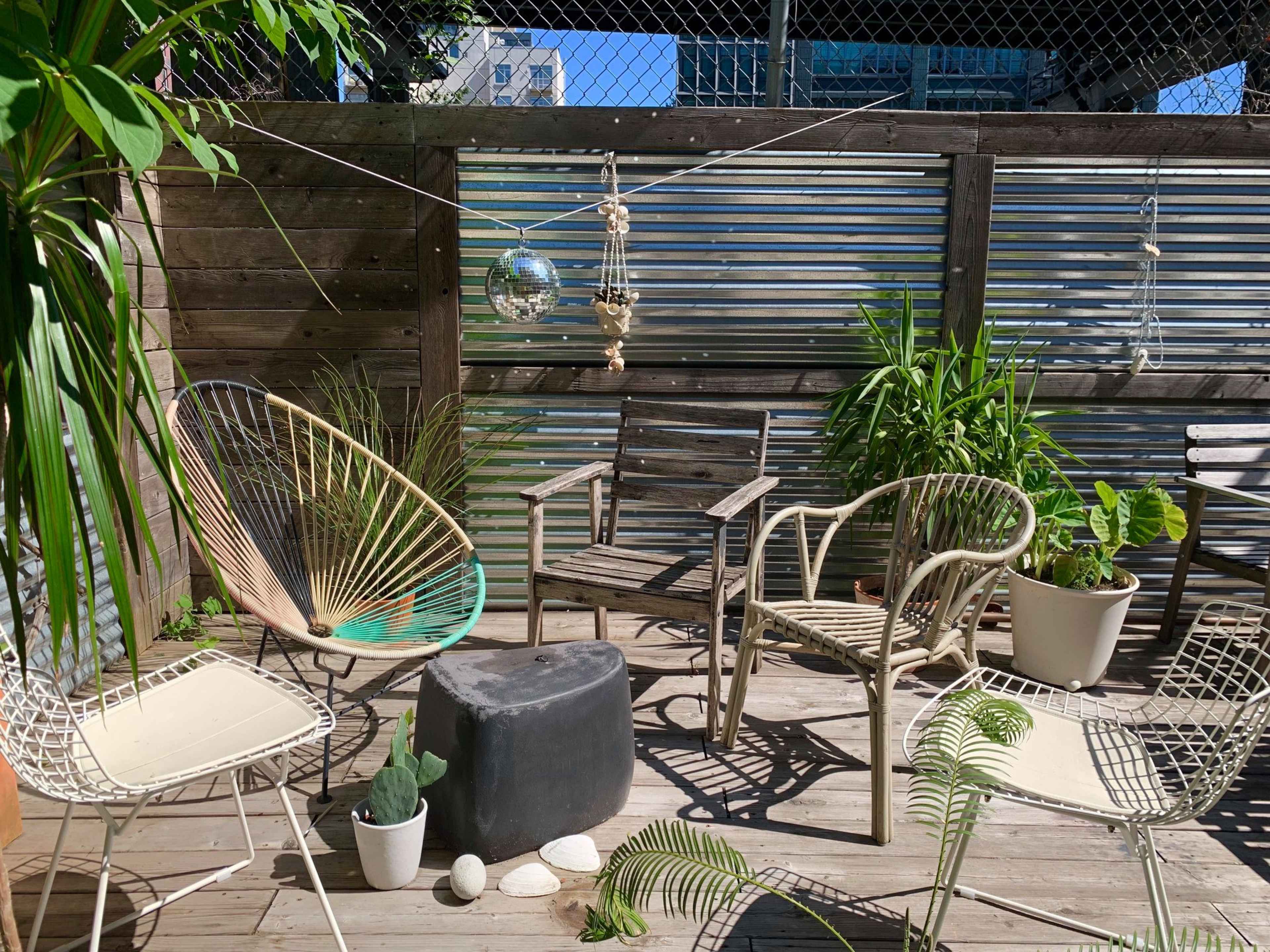 A small outdoor patio features a mix of chairs, a disco ball hanging from a line, and several potted plants surrounded by wooden walls.