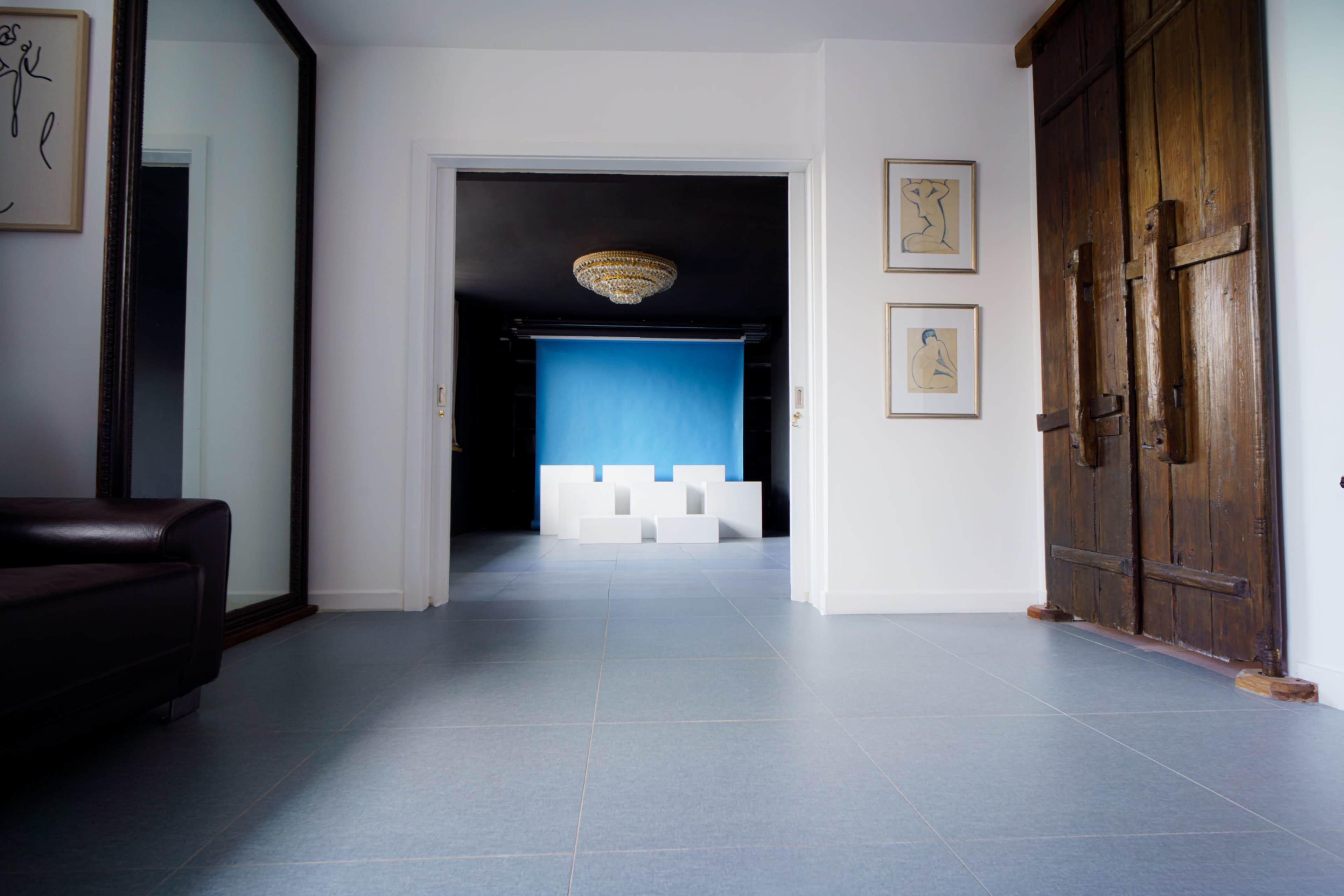 A spacious interior hallway features large wooden doors, a mirror on one wall, and a blue backdrop visible in an adjacent room.