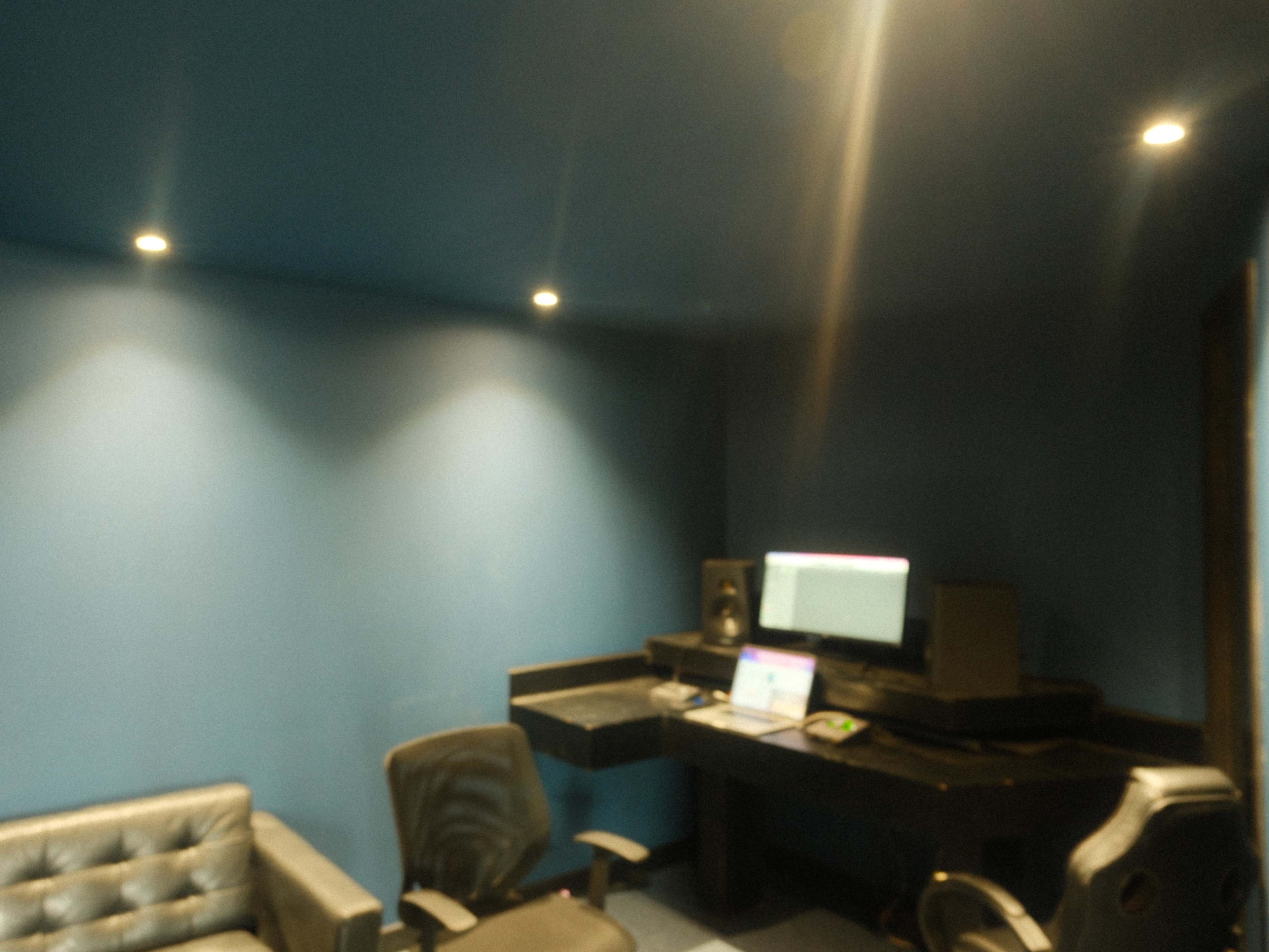 The image shows a music studio with a desk, computer, speakers, and seating arranged against blue walls.
