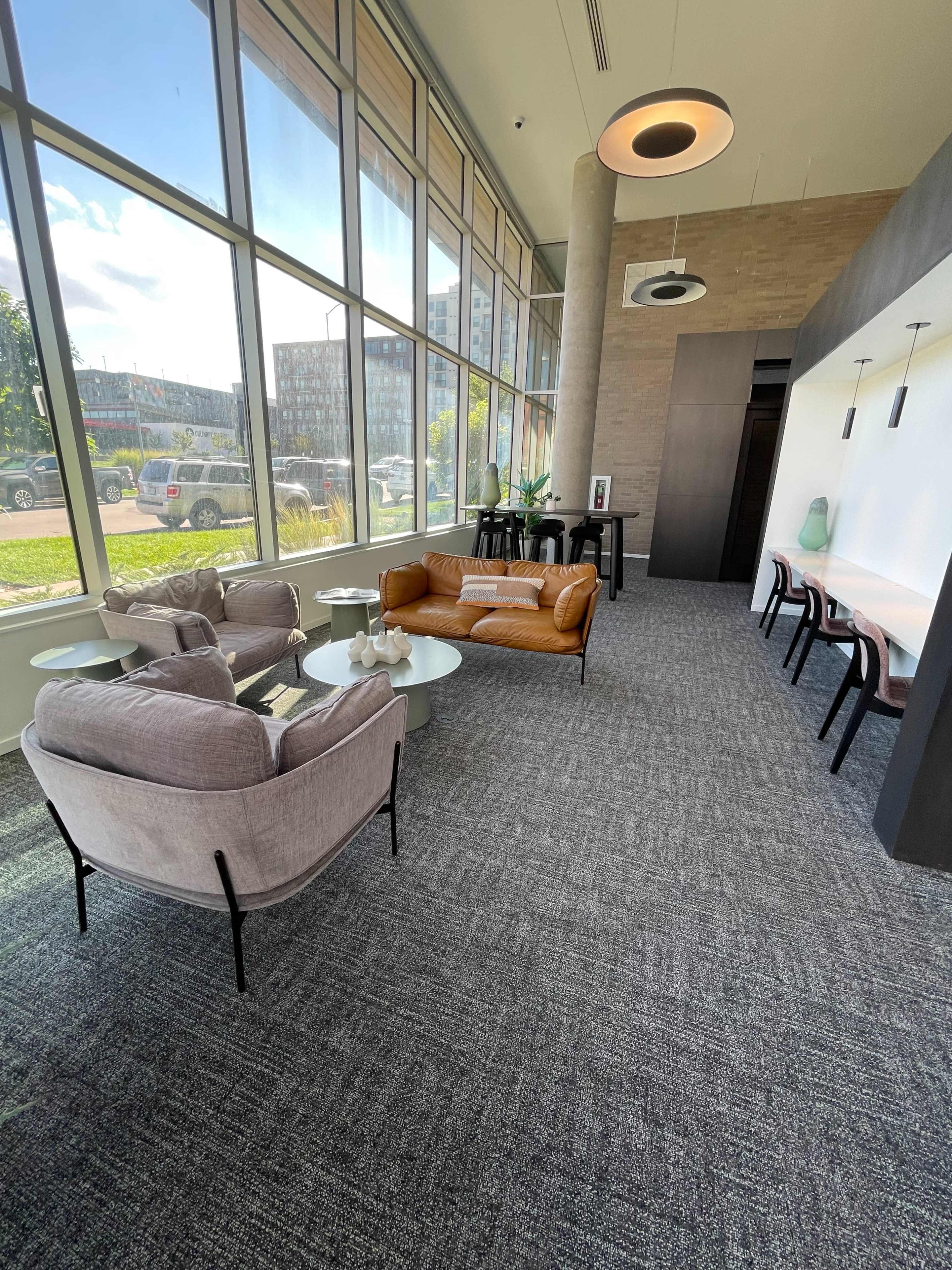 A modern lounge area featuring two sofas, several tables, and large windows allowing natural light.
