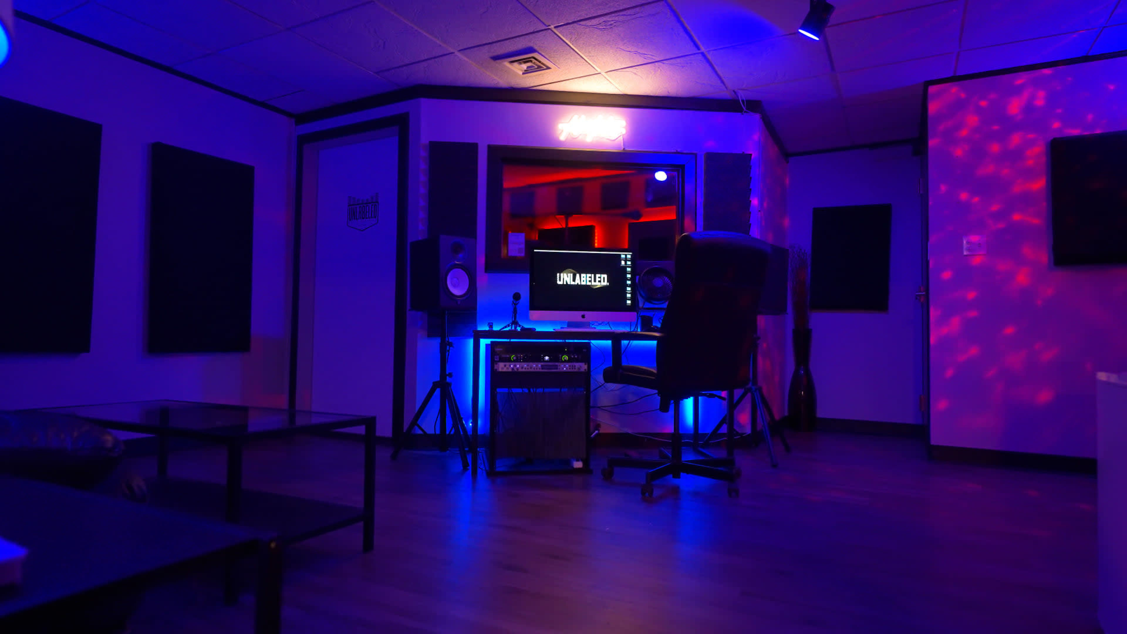 A music recording studio with a computer setup, speakers, and ambient lighting in shades of blue and red.