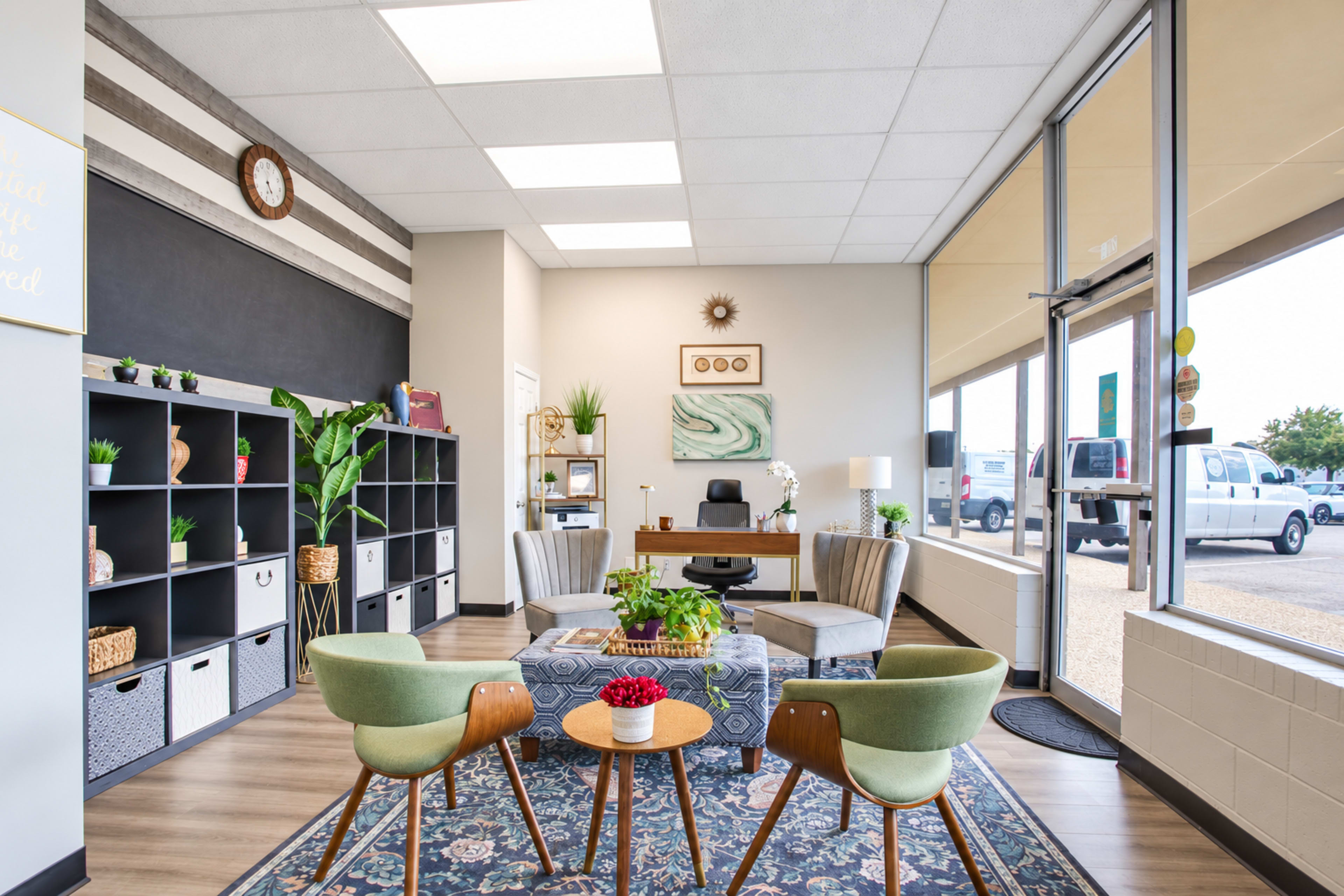 The image shows a modern office reception area featuring a seating arrangement with green chairs and a decorative table, along with shelves and a desk.