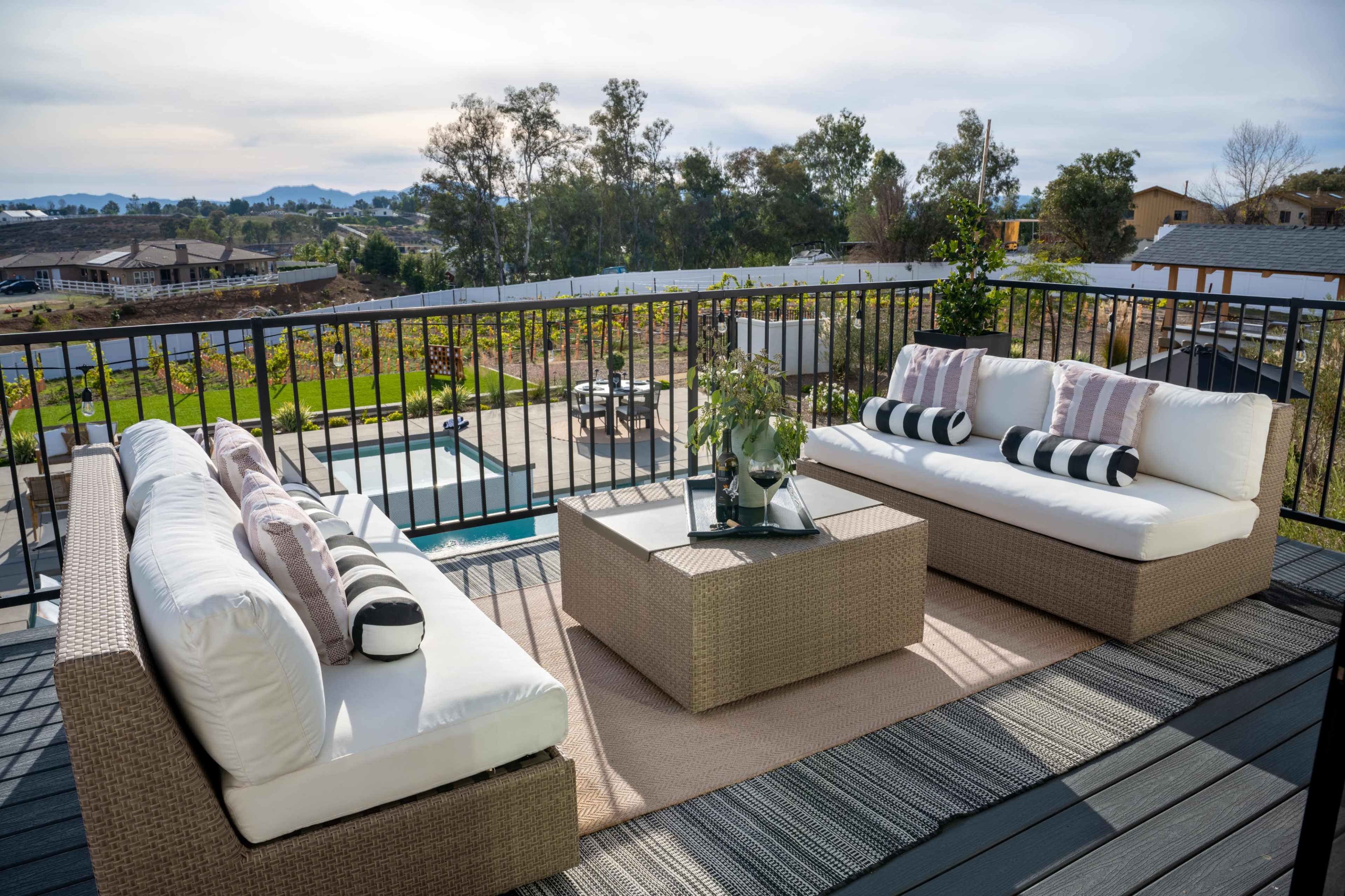 A modern outdoor seating area features two sofas, a coffee table, and a view of a landscaped yard and distant hills.