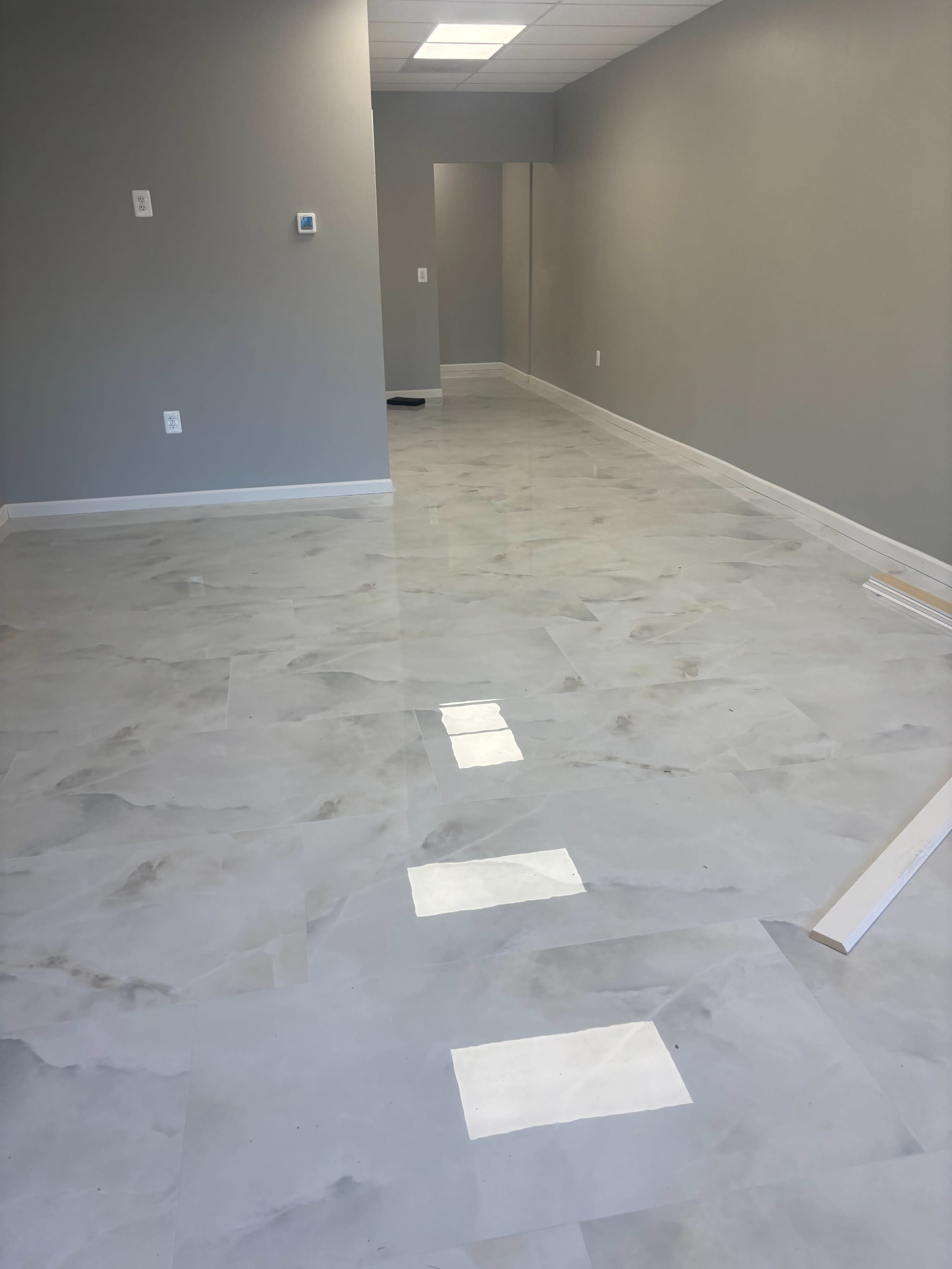 The image shows a polished, light-colored floor with a long corridor leading to a room with gray walls.