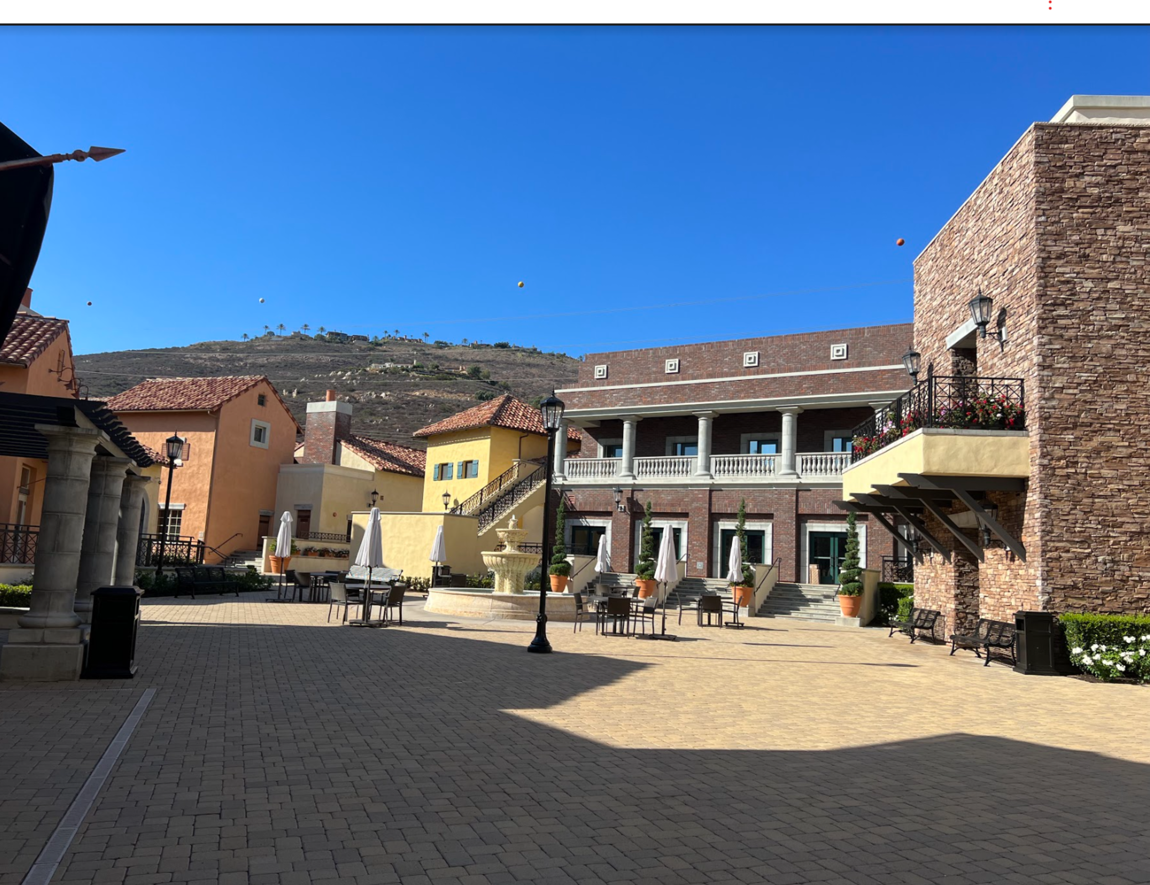 A quaint plaza featuring a mix of colorful buildings, outdoor seating, and a clear blue sky.