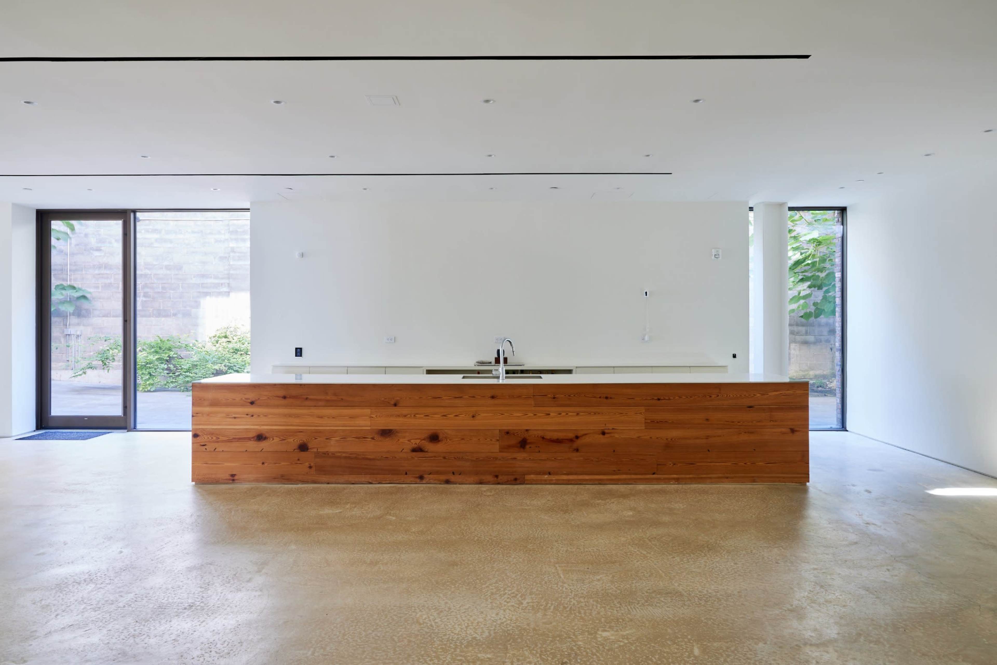 The image shows a modern kitchen with a wooden island and a minimalist design, featuring large windows that allow natural light to enter.