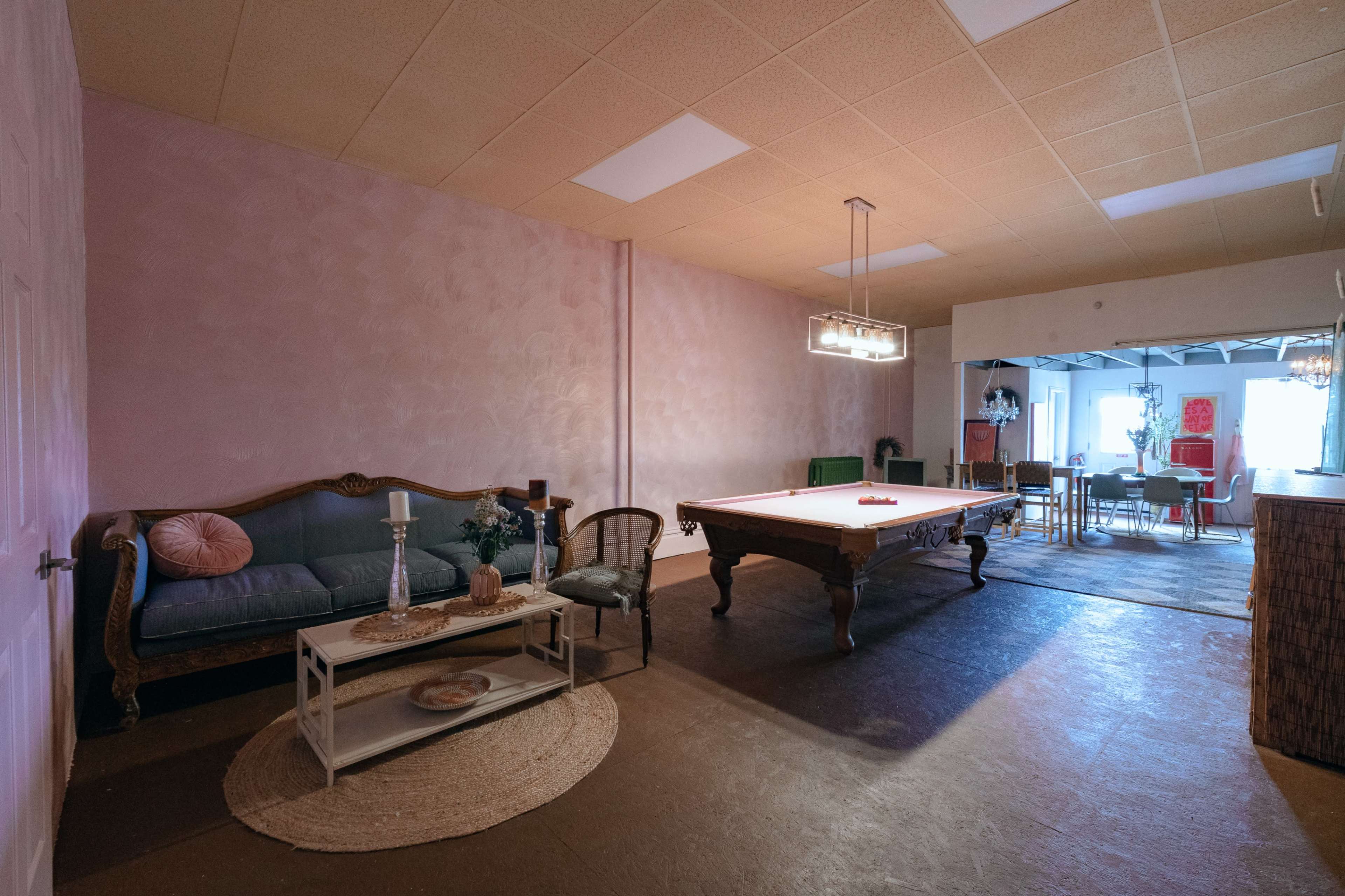 An interior space featuring a billiard table, a seating area with a couch and coffee table, and a dining area in the background.