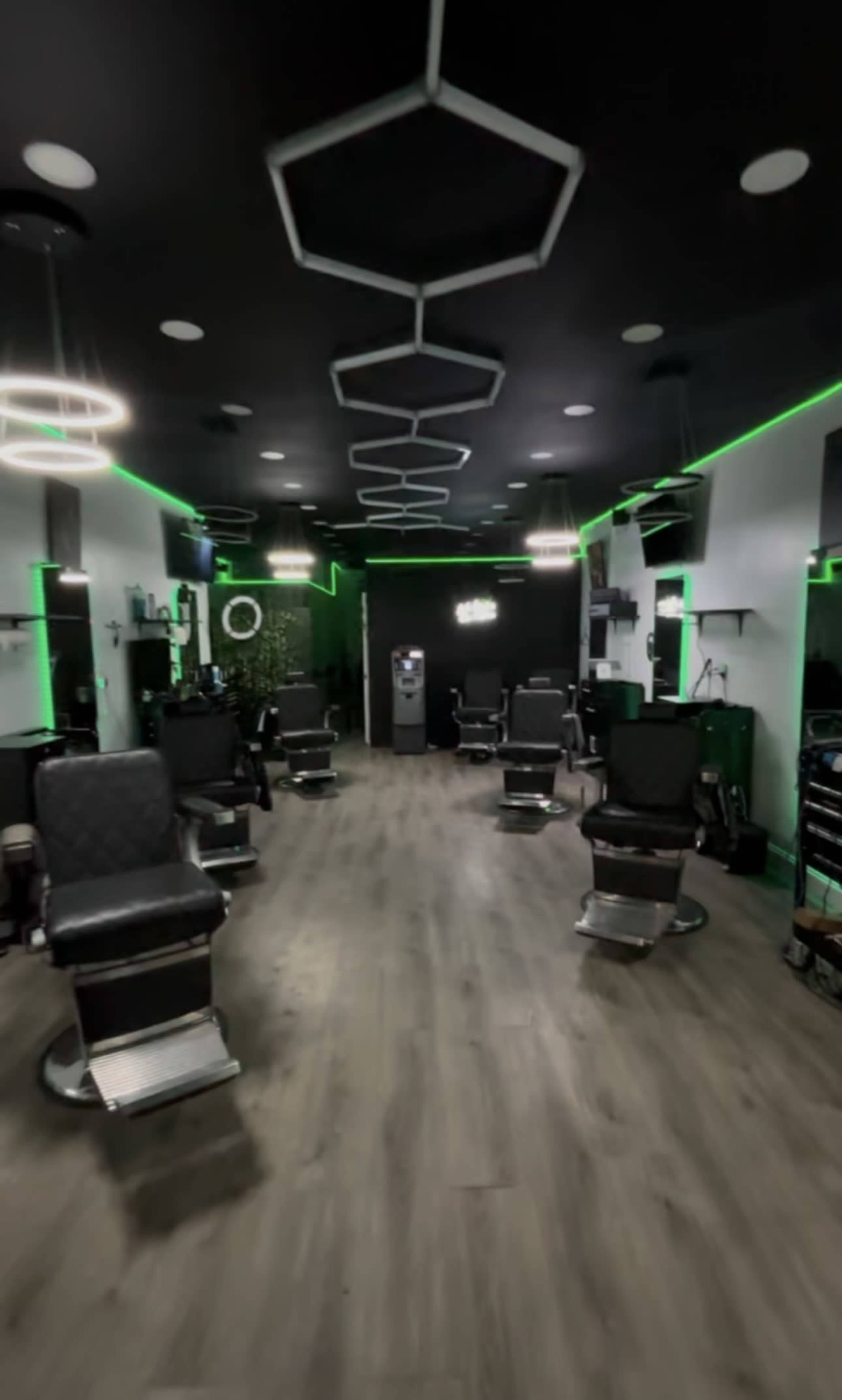 The image shows an interior of a modern barbershop with several barber chairs arranged along the walls and green LED lighting.