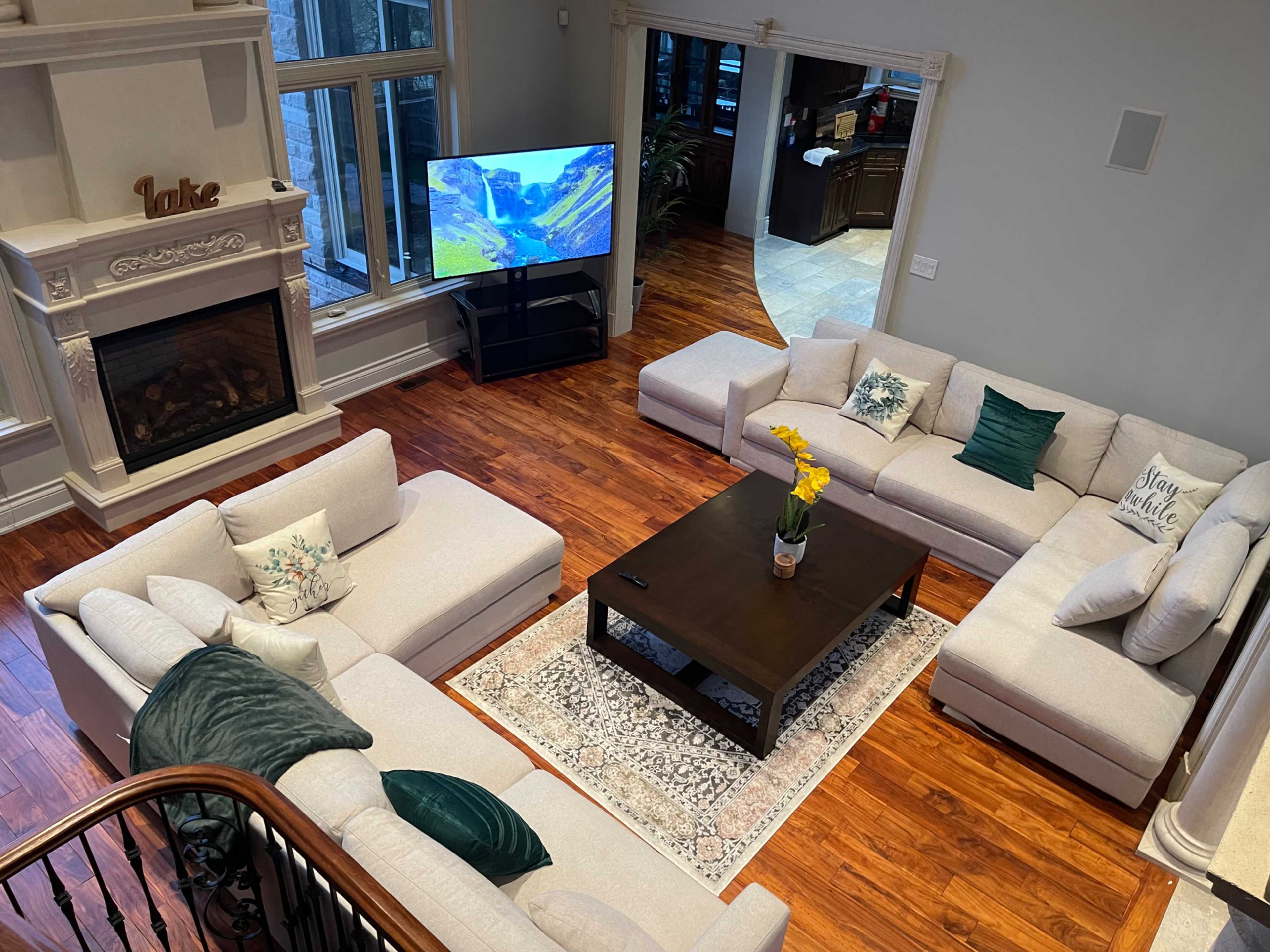 A spacious living room with two sectional sofas arranged around a dark coffee table, complemented by a patterned area rug and a television displaying a landscape scene.
