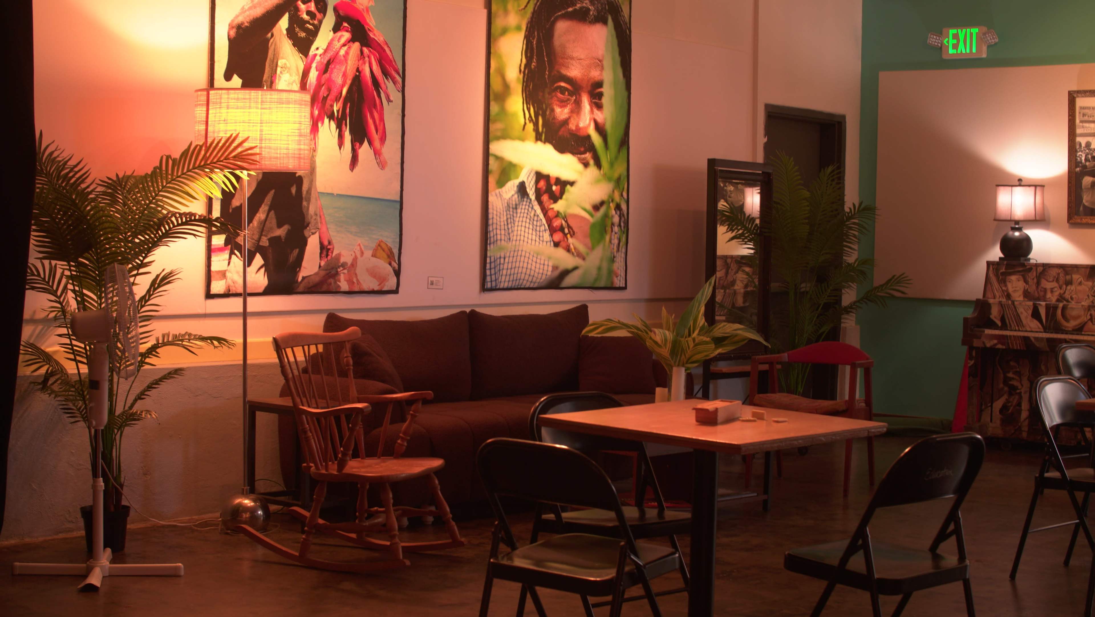 The scene features a cozy interior with a brown sofa, a wooden table, and chairs, adorned with vibrant wall art and plants.