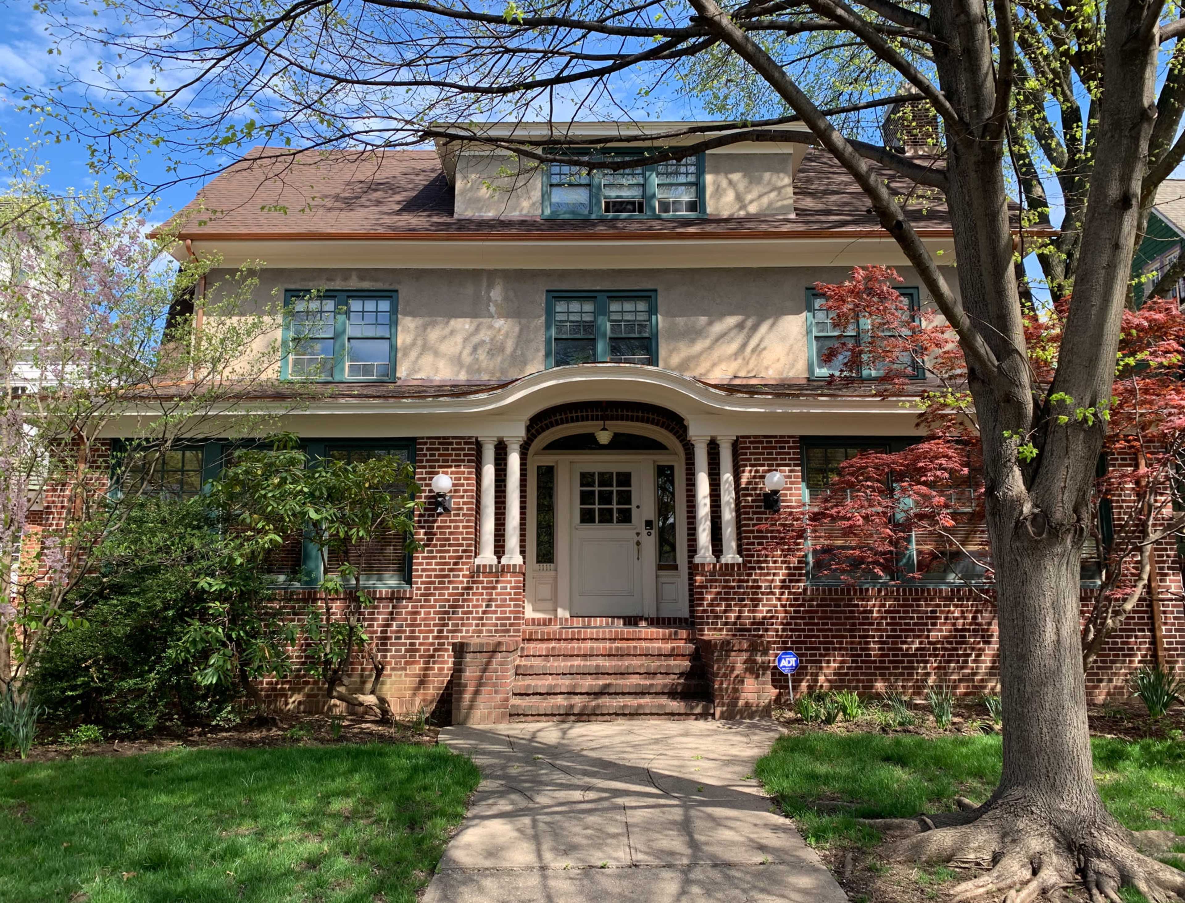 A large brick house with a tan upper facade, a front porch supported by white columns, and a neatly landscaped yard.