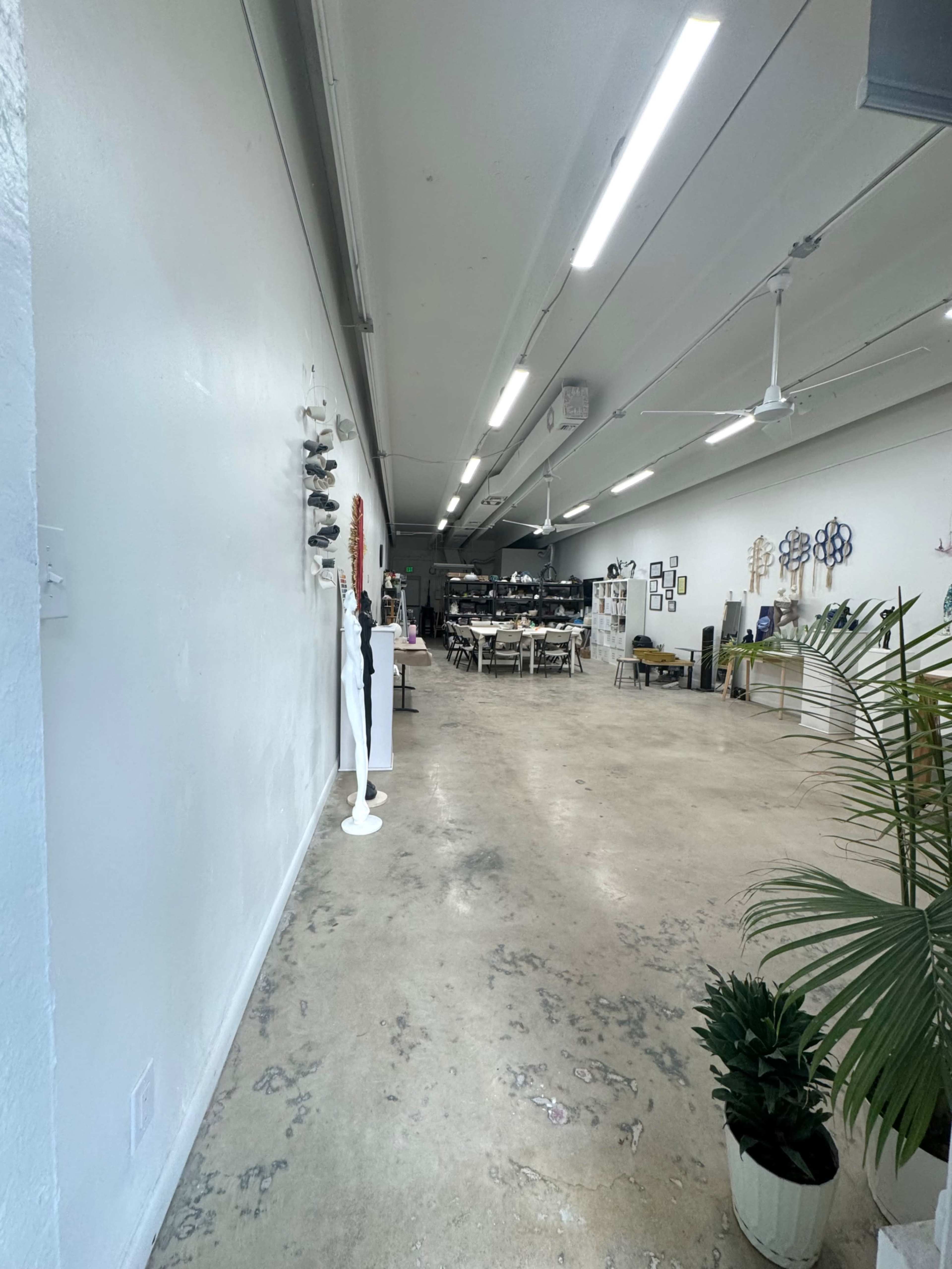 The image shows a long, narrow room with polished concrete flooring, white walls, and various decorative items displayed along one side.